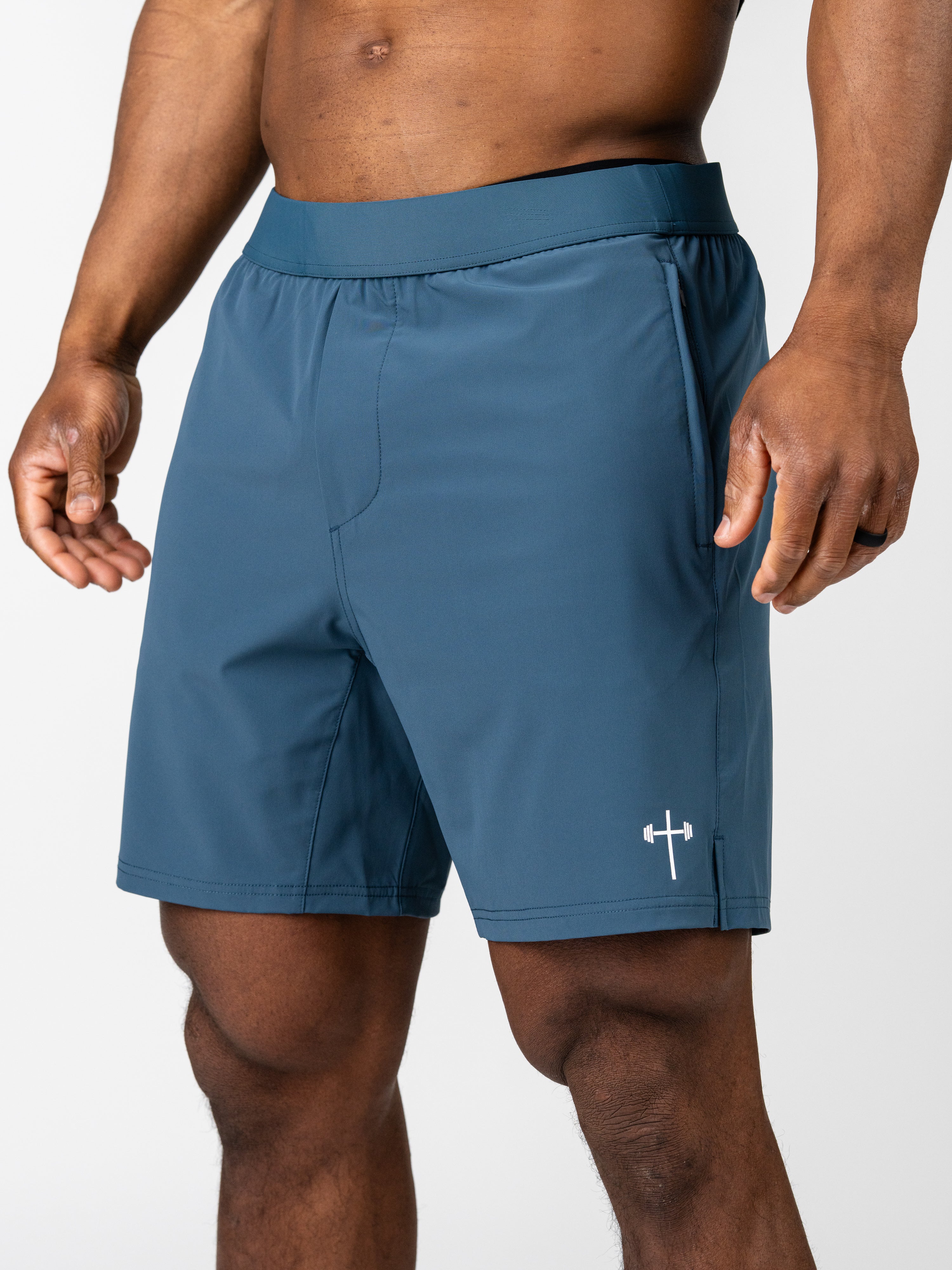 Man wearing blue Essential Training Shorts with a small white cross and barbell logo on the left leg, designed for lightweight, breathable performance during workouts.
