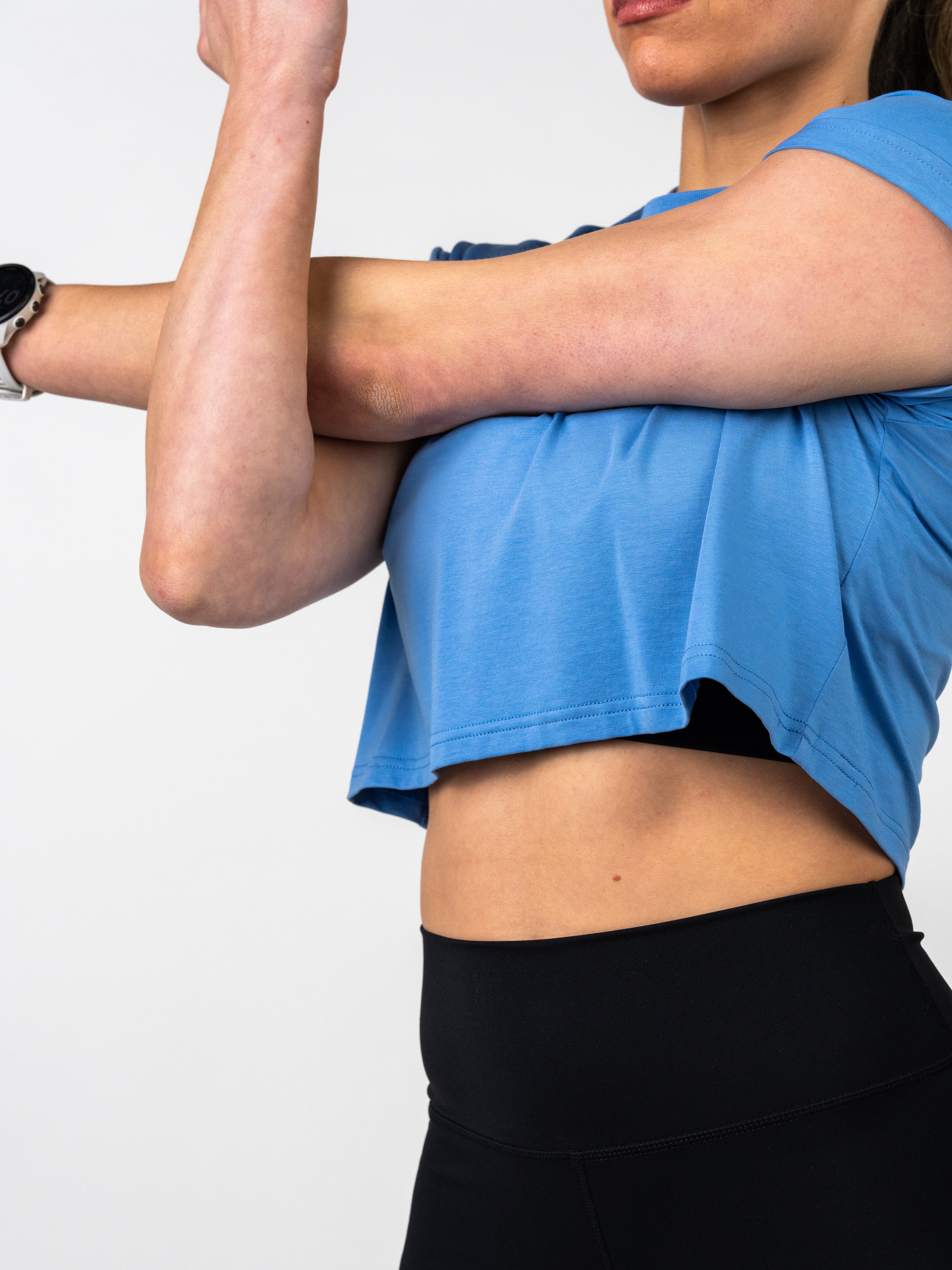 Close-up of a person stretching their arm wearing a light blue Jesus is King Essential Crop Tee paired with black high-waisted athletic leggings, showcasing faith-based fitness apparel.