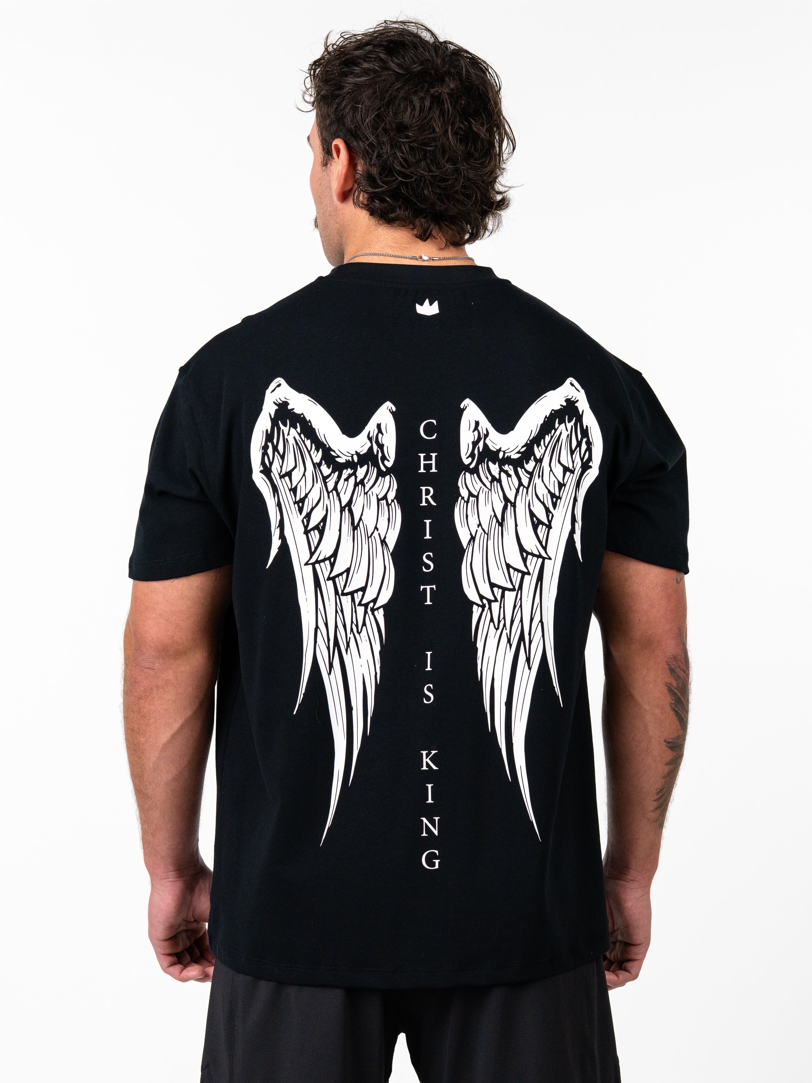 Person wearing a black t-shirt with angel wings and 'Christ is King' text on the back.