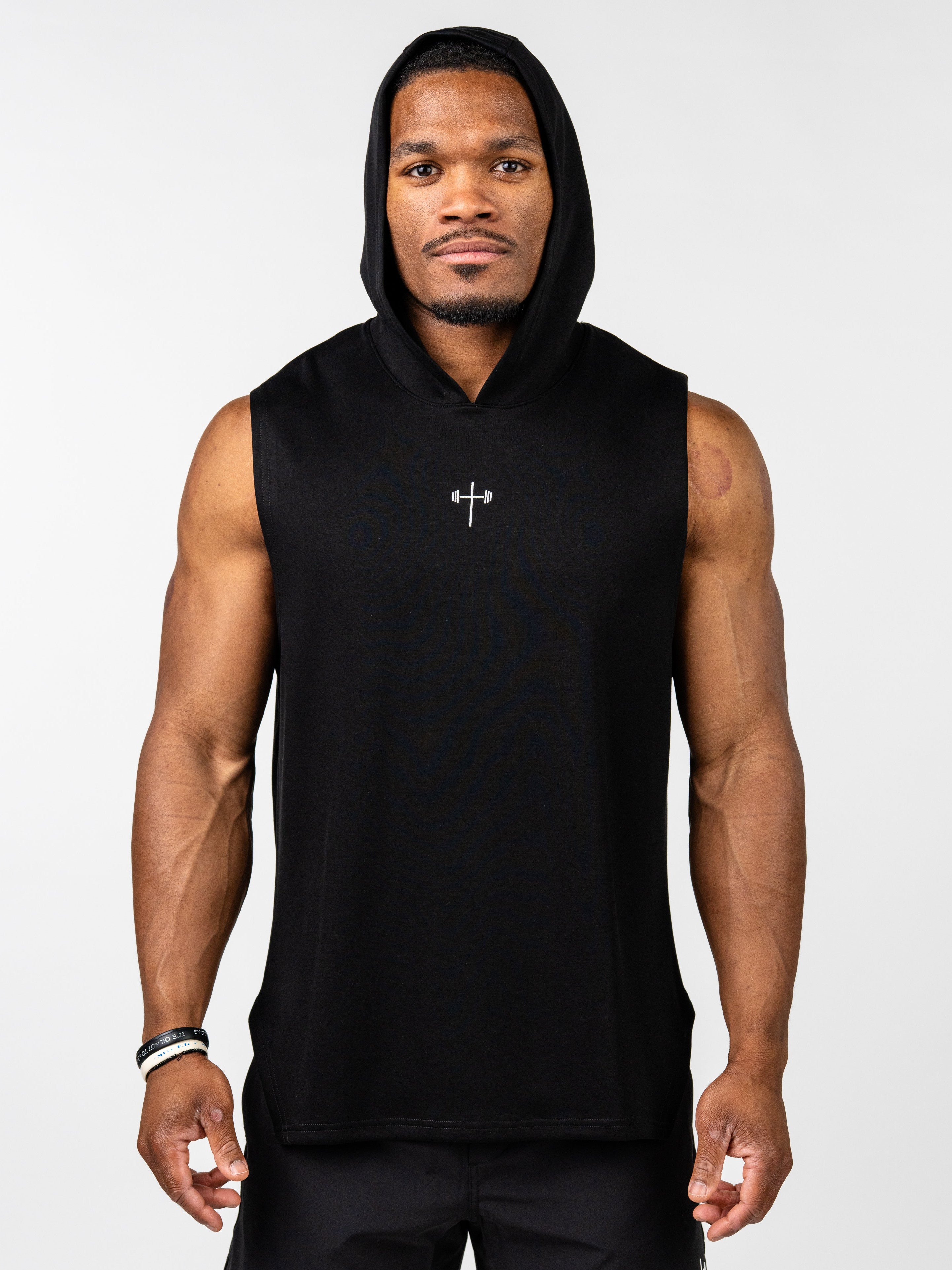 Man wearing a black Essential Sleeveless Hoodie with a hood and a small silver cross and barbell design on the chest, styled for Christian fitness apparel.