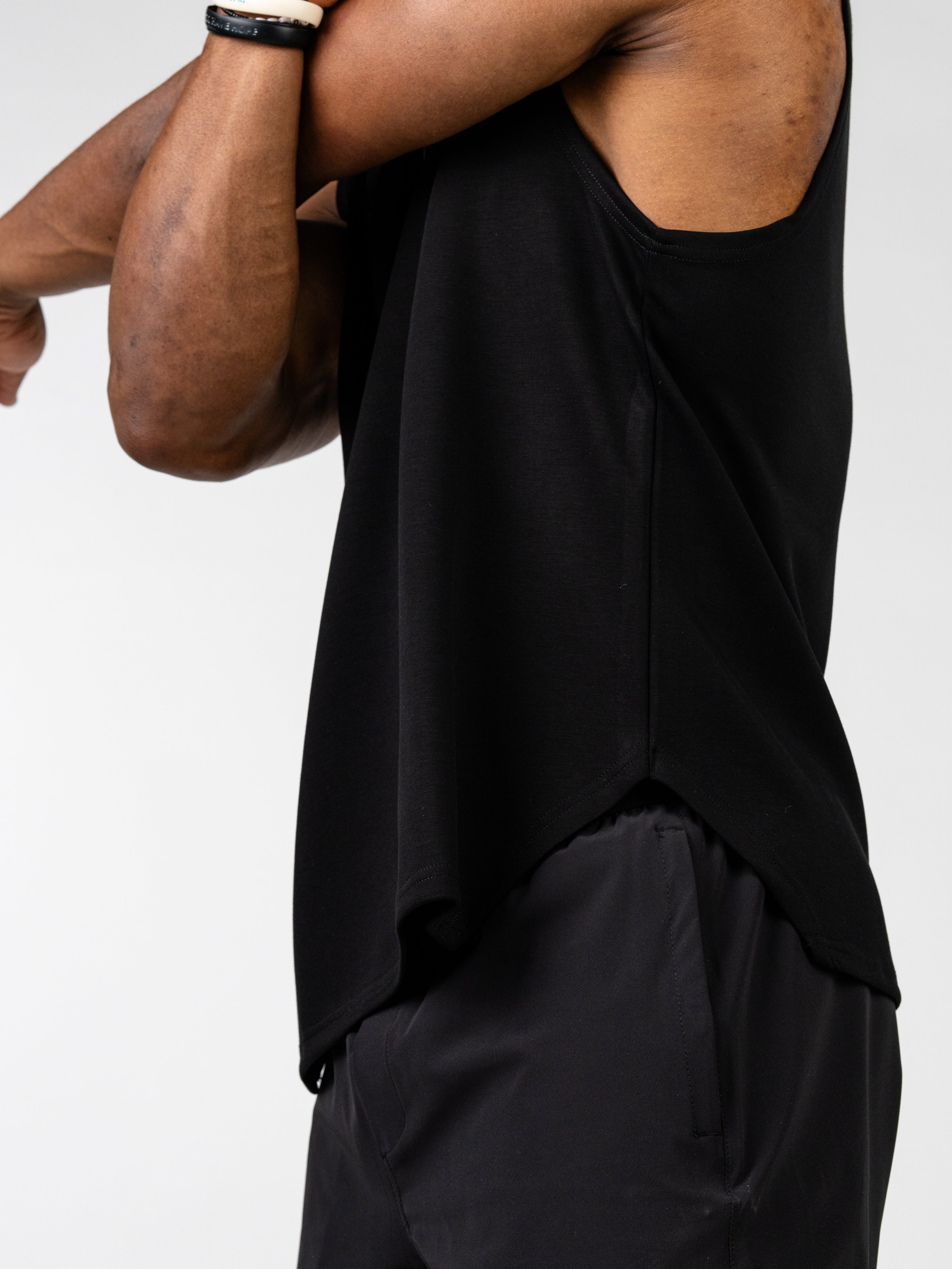 Athlete wearing a black Essential Sleeveless Hoodie stretching arms, showcasing sleeveless design and lightweight fabric ideal for unrestricted movement during workouts.
