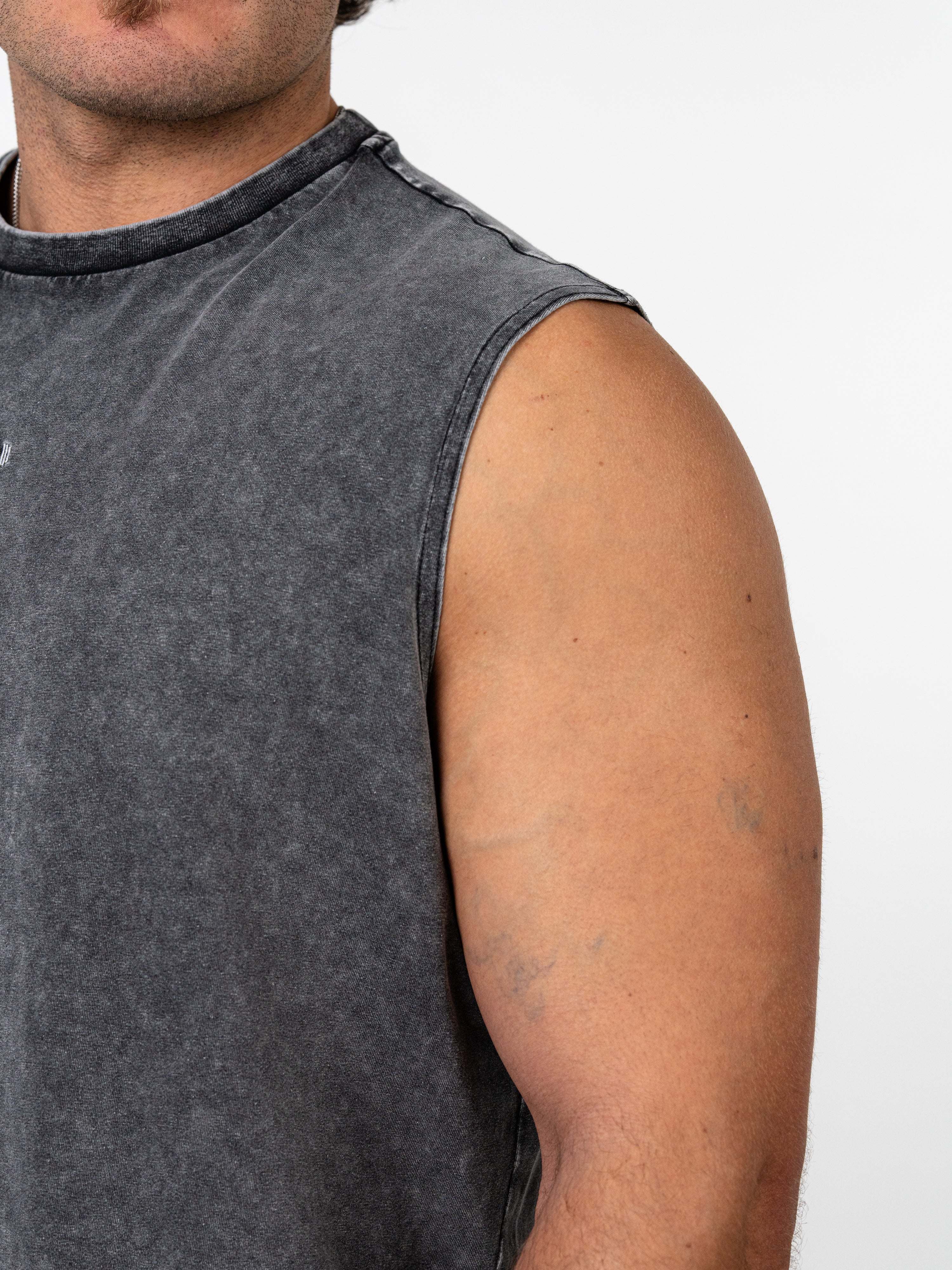 Close-up of a man's upper arm and shoulder wearing a dark gray Servant of God Vintage Premium Tank, a sleeveless Christian fitness apparel with a washed vintage look.