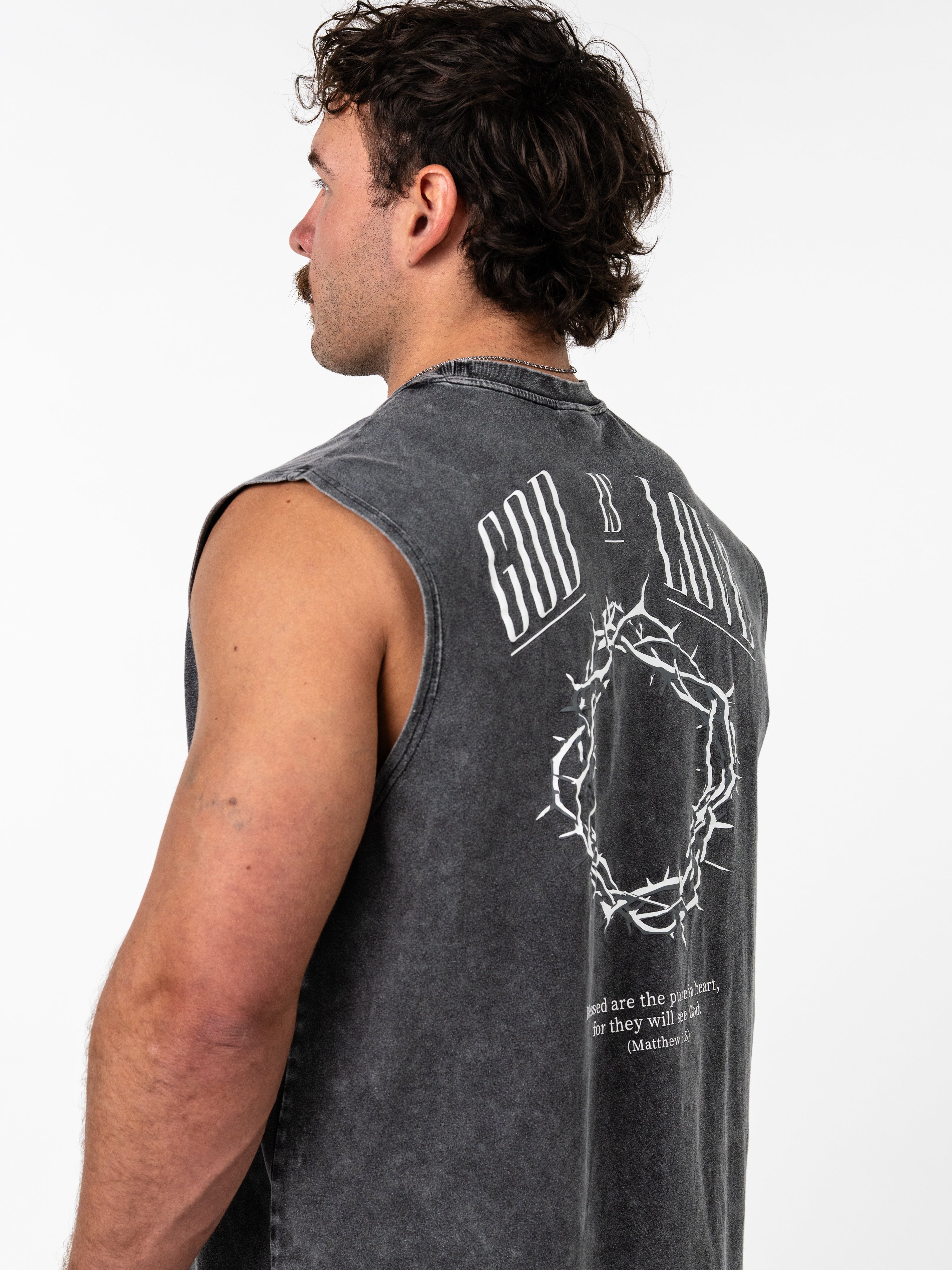 Man wearing a faded black God is Love Vintage Premium Tank featuring a crown of thorns graphic and a Bible verse on the back, showcasing Christian fitness apparel.