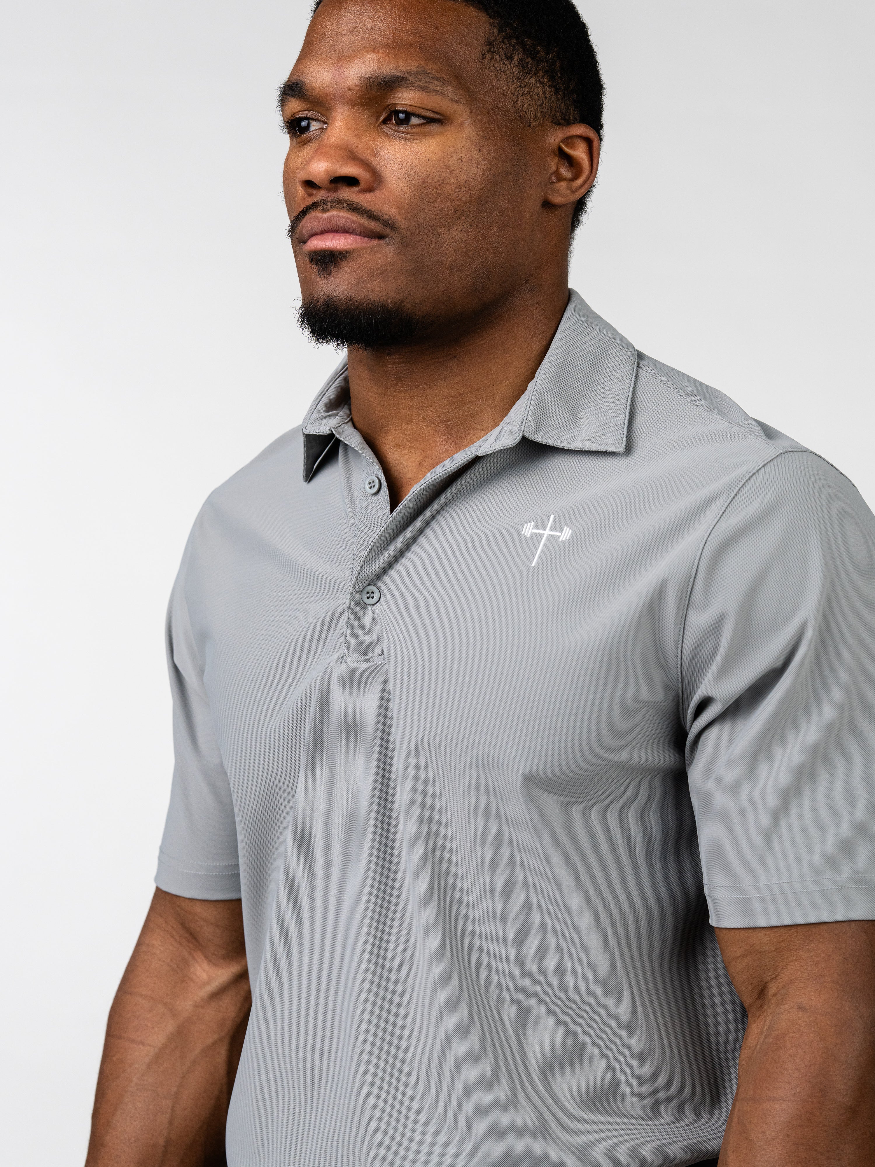 Man wearing a light gray Core Athletic Polo featuring a subtle Christian barbell cross logo on the chest, designed for comfort and performance in faith-based fitness apparel.
