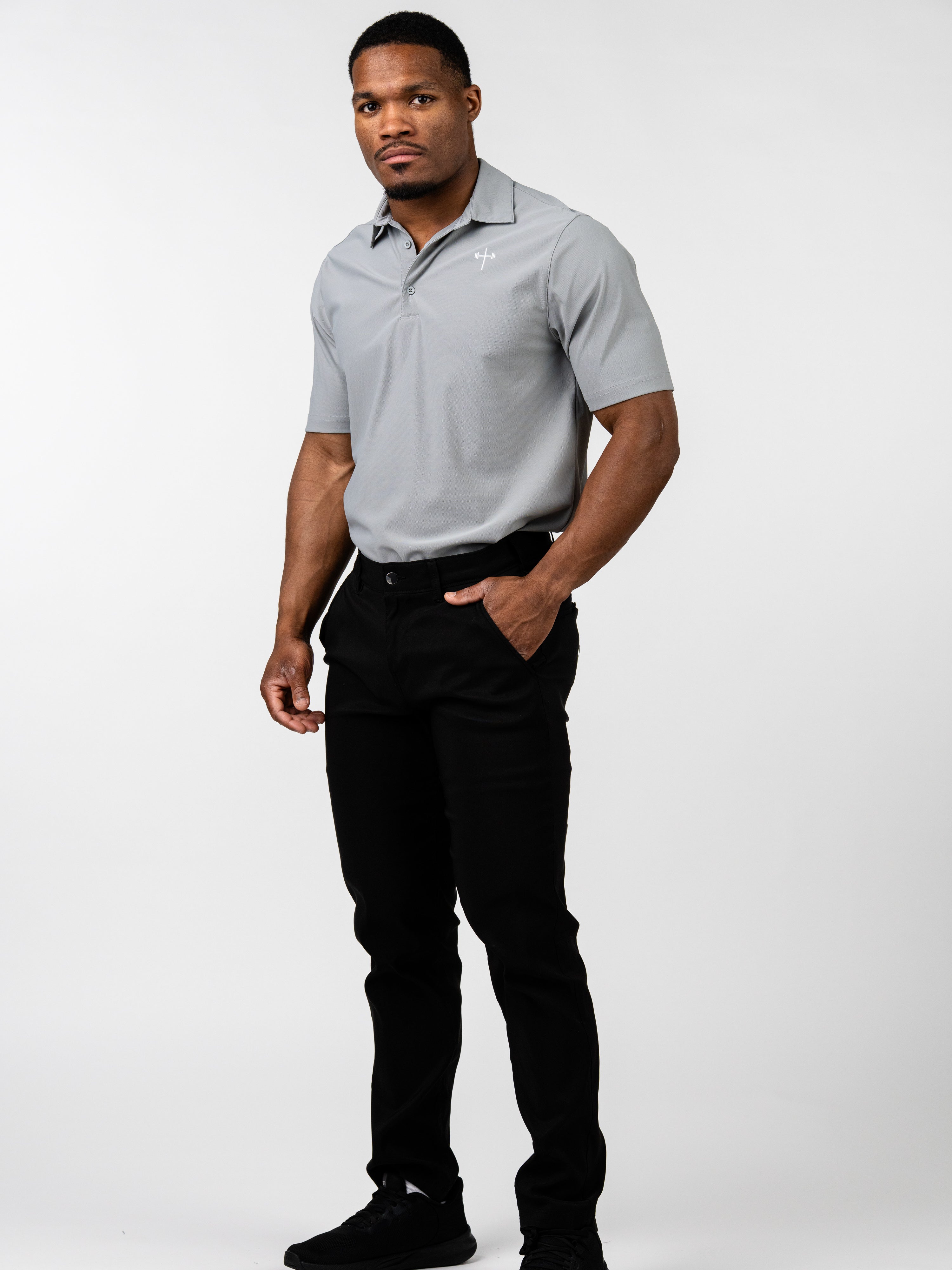 Man wearing a grey Core Athletic Polo with a subtle Christian cross and barbell design, paired with black pants, standing against a plain white background.