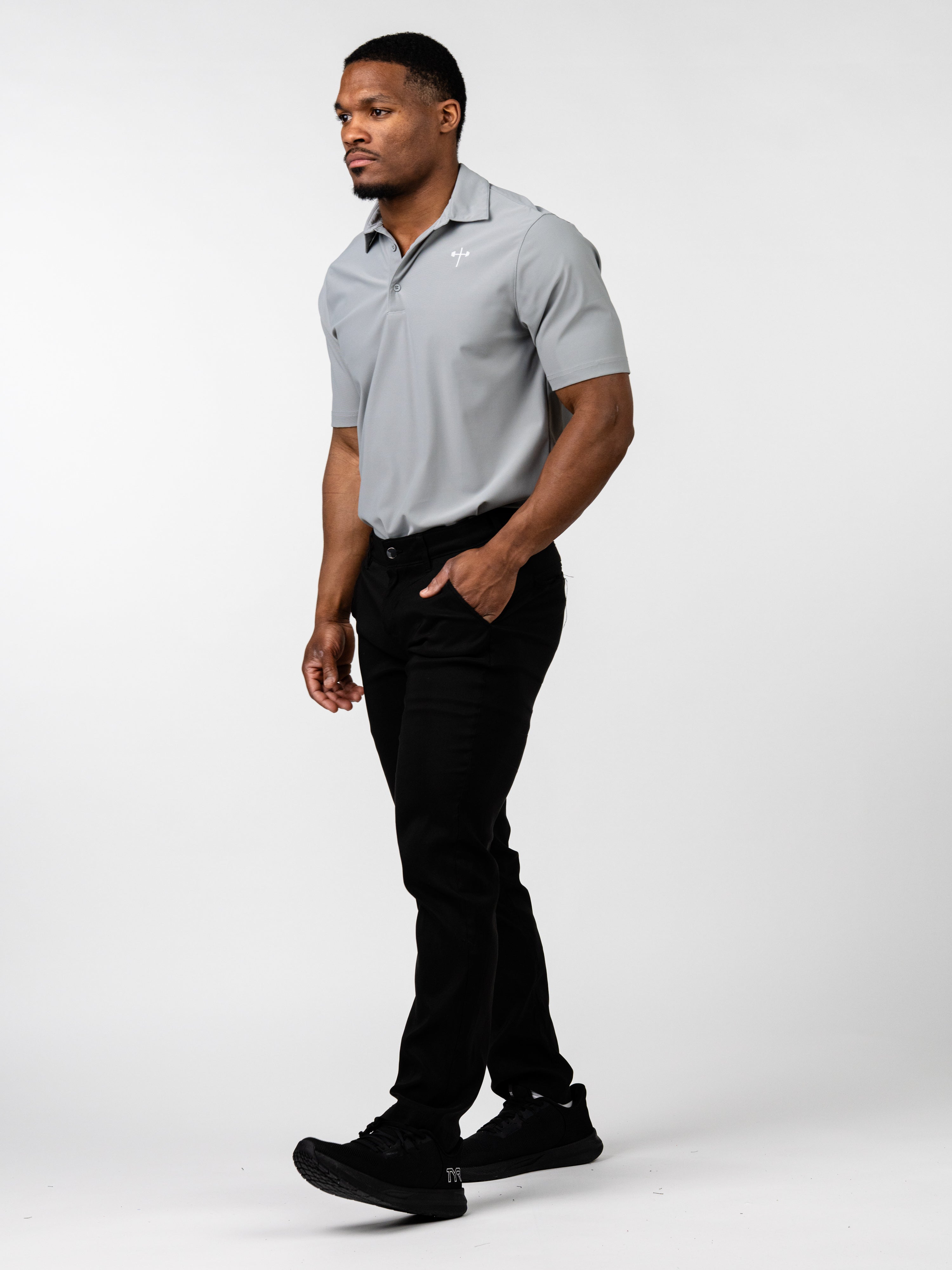Man wearing a gray Core Athletic Polo with a subtle Christian cross logo on the chest, paired with black pants and black athletic shoes, standing against a plain background.