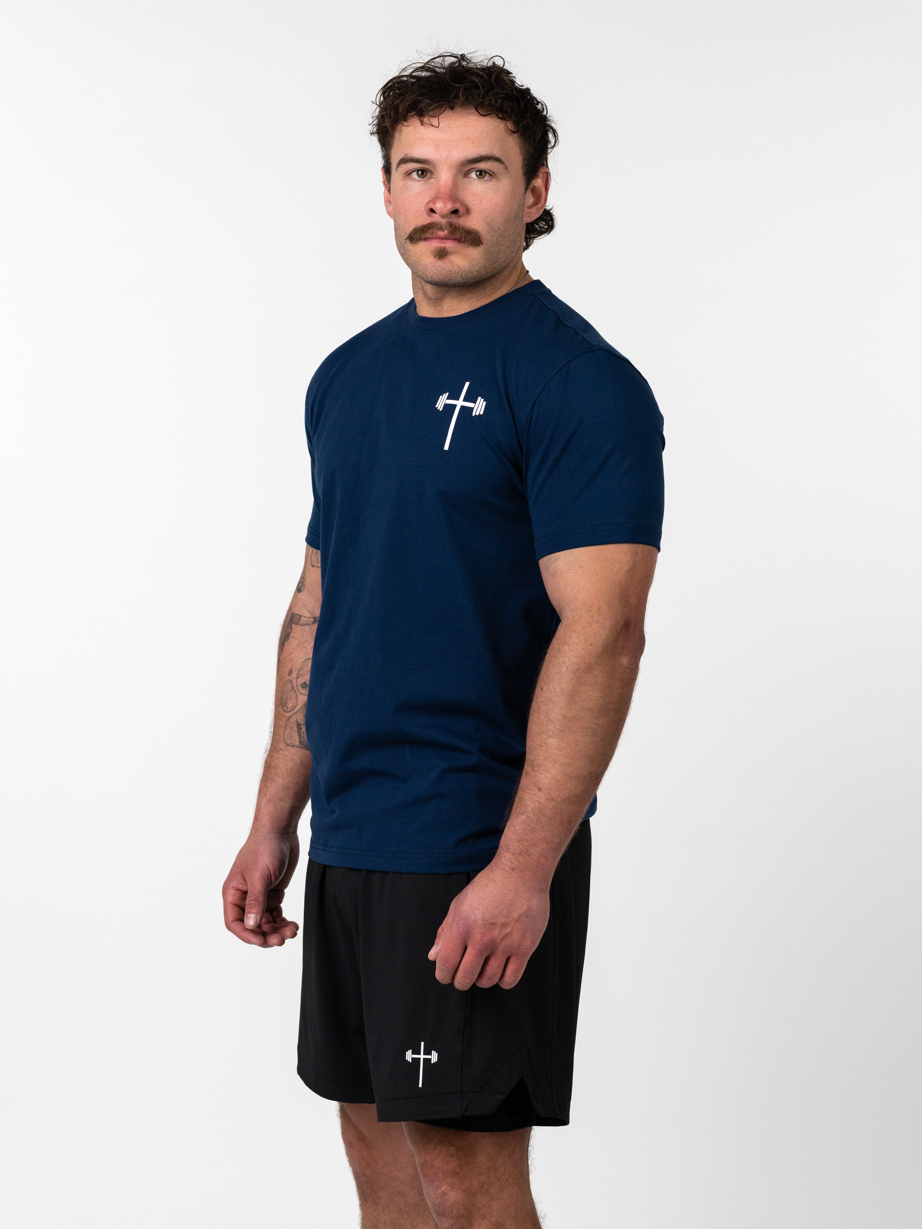 Man wearing a navy blue Kingdom Performance Tee with a small white cross and barbell logo on the chest, paired with black shorts featuring the same logo.