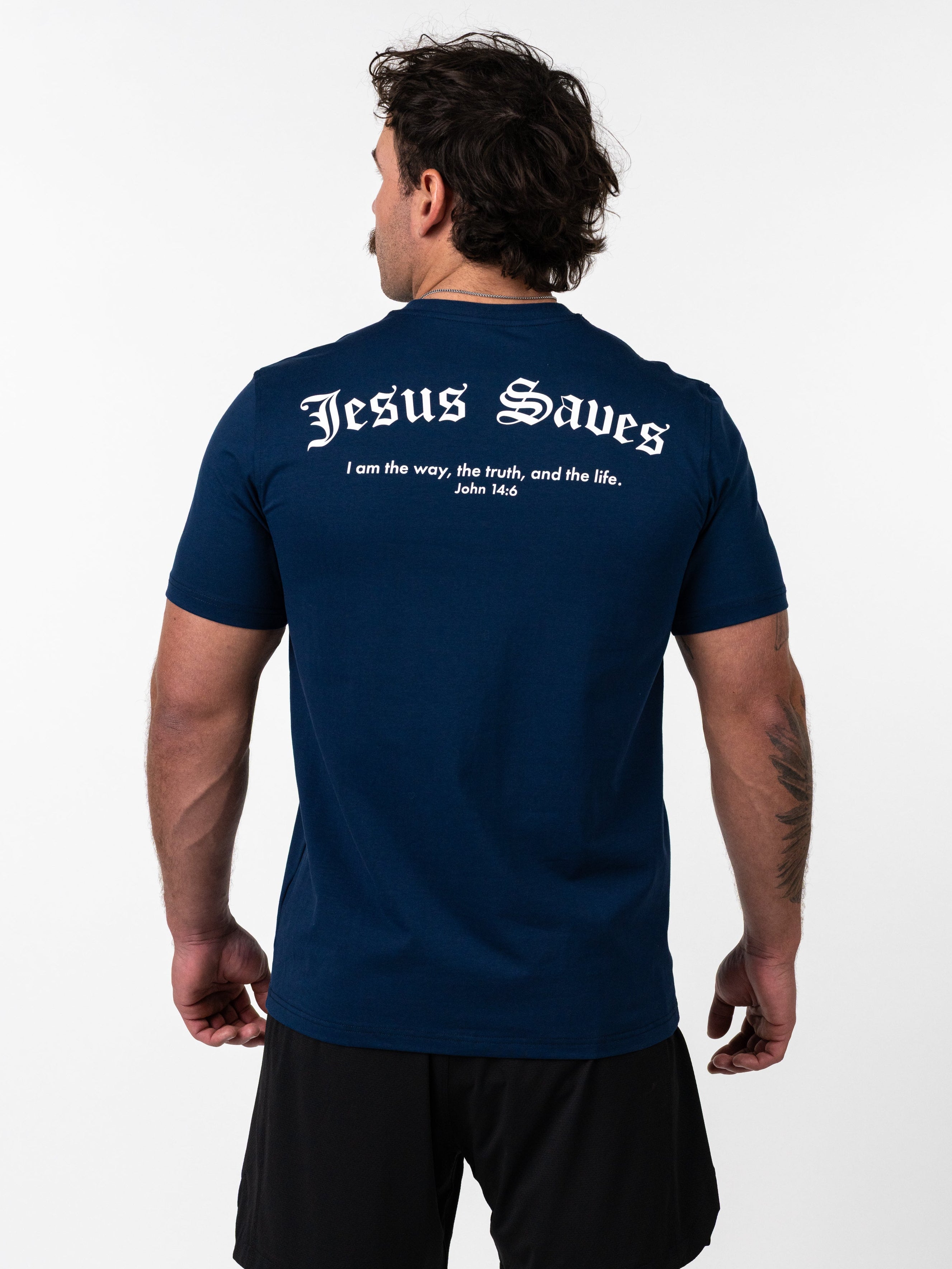 Man wearing a navy blue Kingdom Performance Tee with "Jesus Saves" and a Bible verse printed on the back, paired with black shorts, shown from behind.