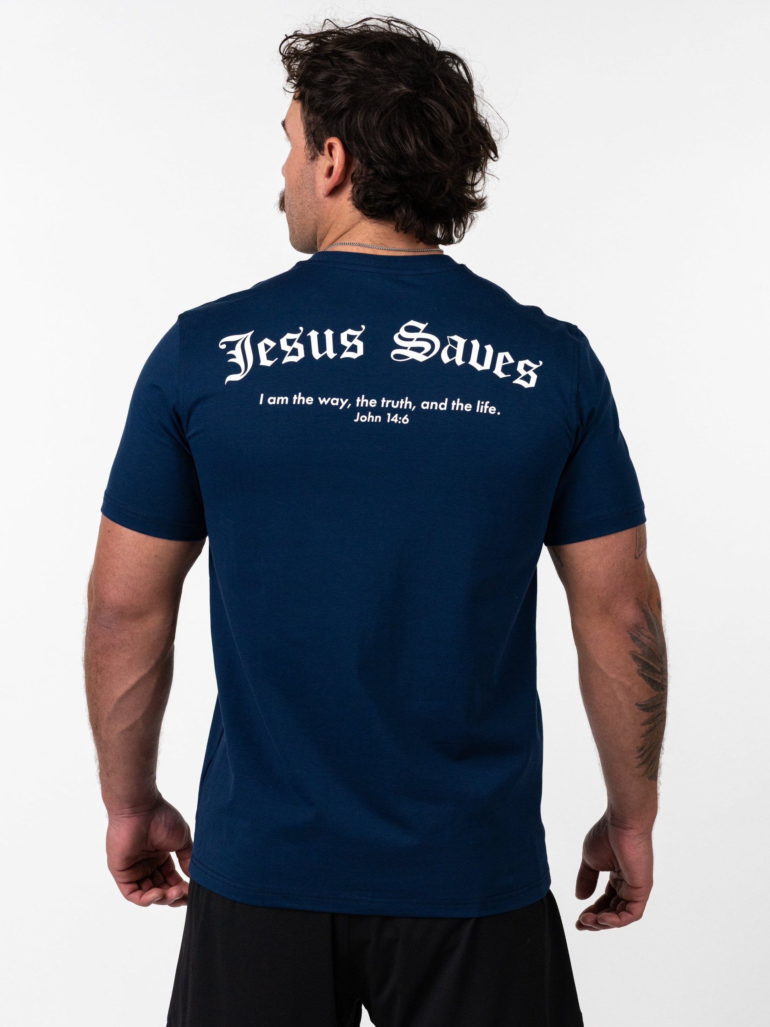 Man wearing a navy blue Kingdom Performance Tee with "Jesus Saves" and a Bible verse printed on the back, paired with black shorts, shown from behind.