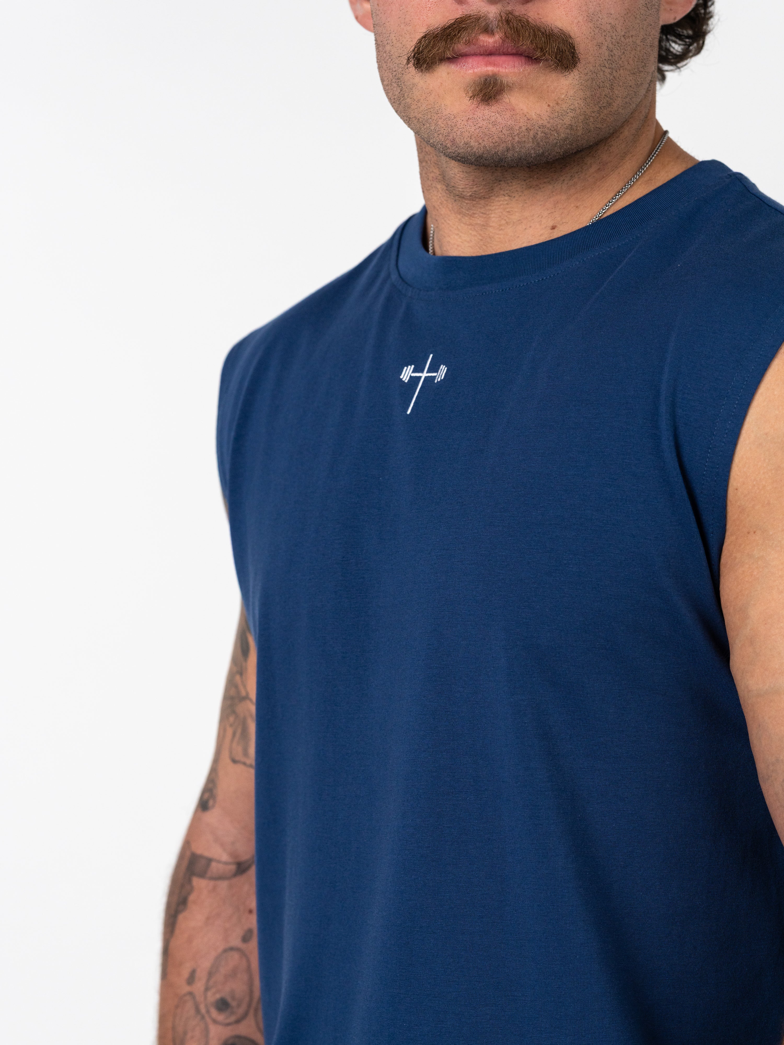 Man wearing a navy blue Scripture Premium Sleeveless Tank with a small white cross and barbell design on the chest, showcasing Christian fitness apparel.