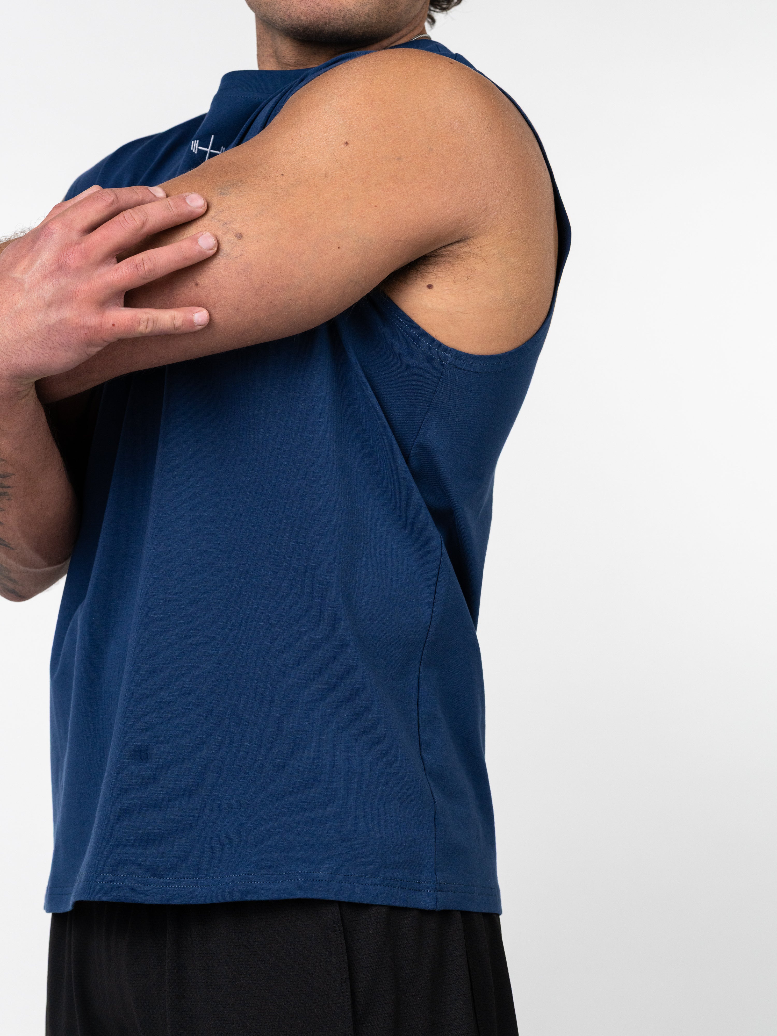 Man wearing a navy Scripture Premium Sleeveless Tank stretching his arm, showcasing the athletic fit and fabric, designed for Christian fitness apparel and activewear.