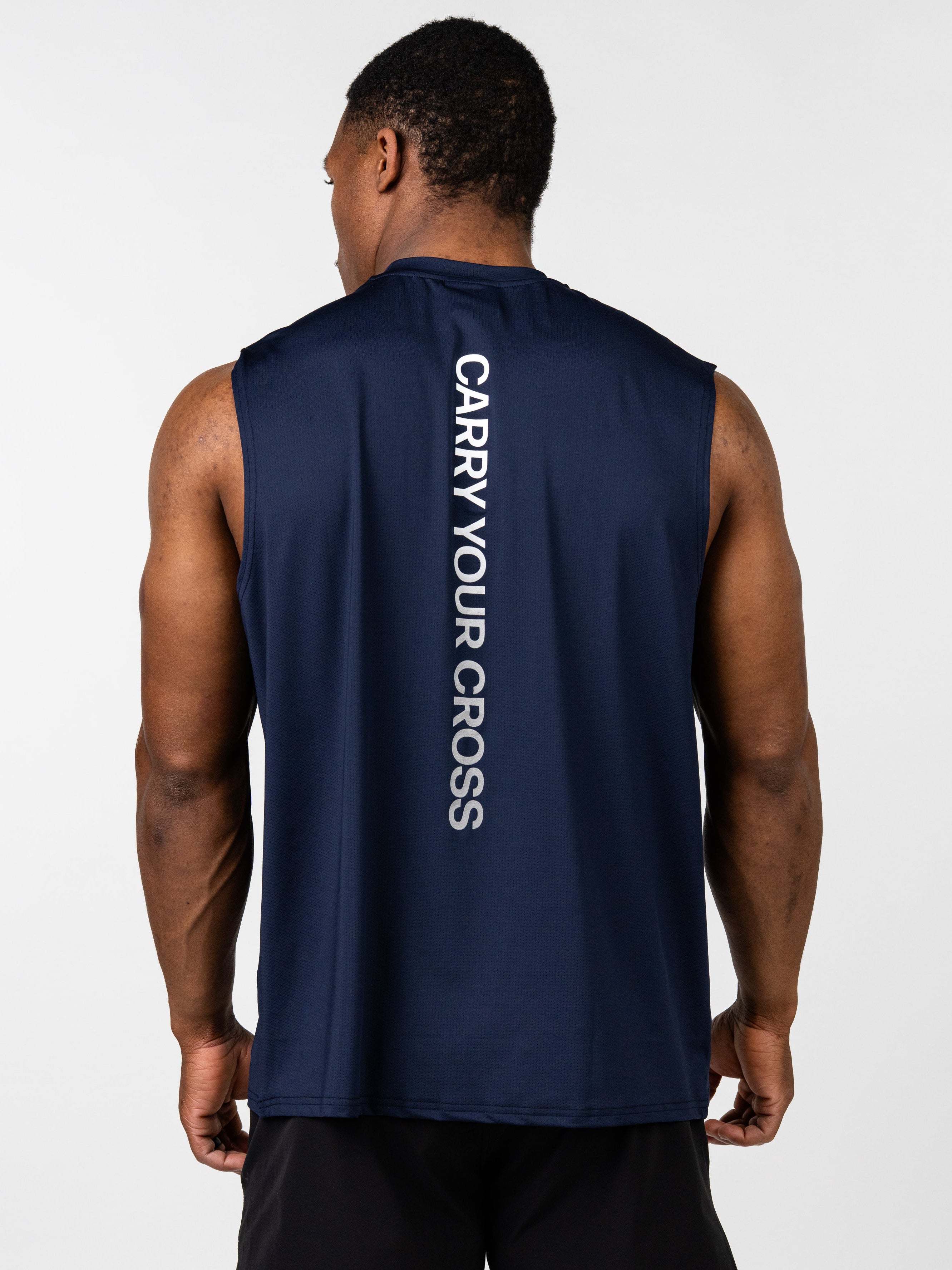 Man wearing a navy blue Carry Your Cross Premium Oversized Tank with white vertical text on the back, paired with black athletic shorts, showcasing a faith-based fitness apparel style.
