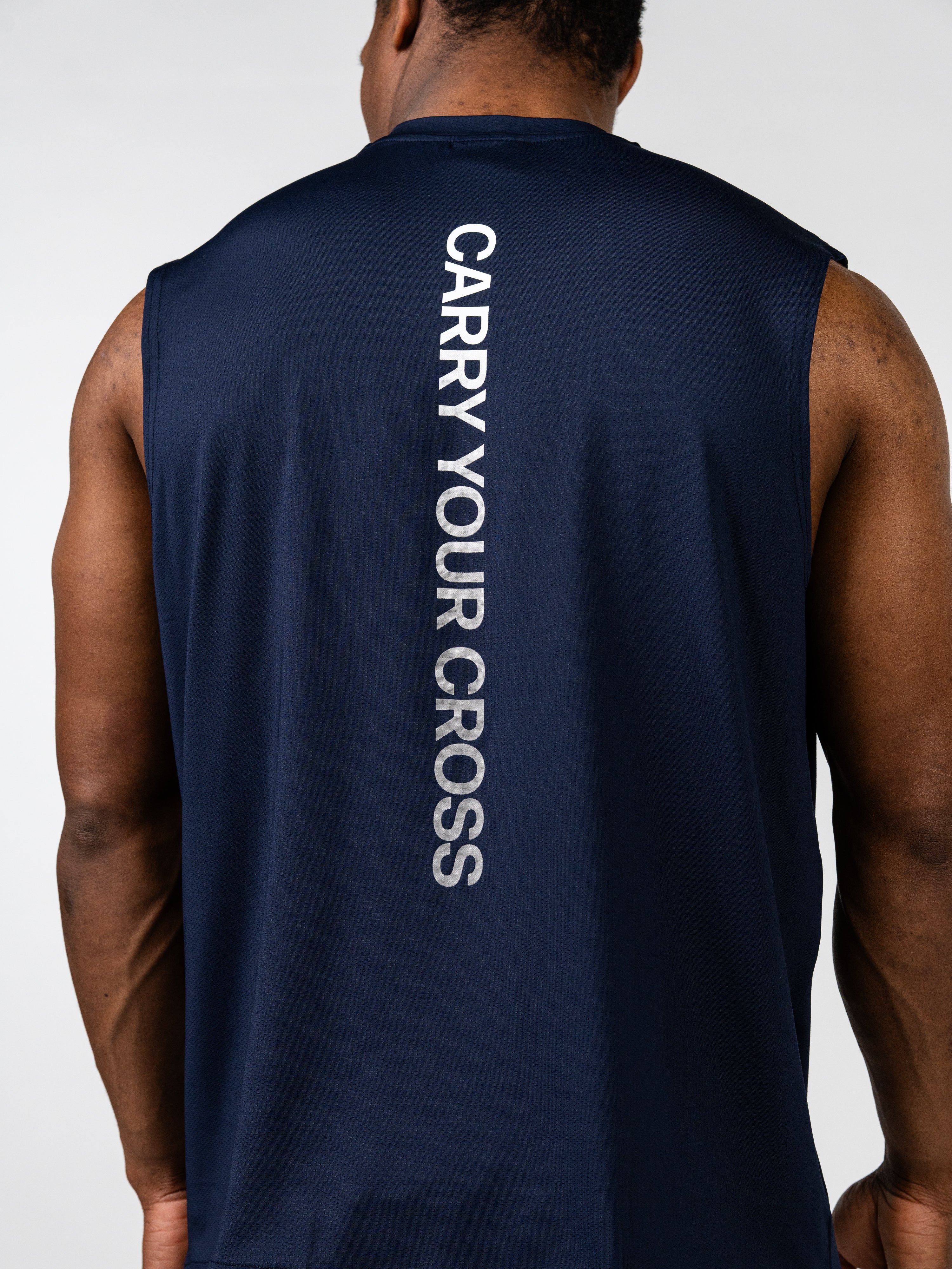 Man wearing a navy blue Carry Your Cross Premium Oversized Tank with bold vertical white text on the back, designed for Christian fitness and activewear.