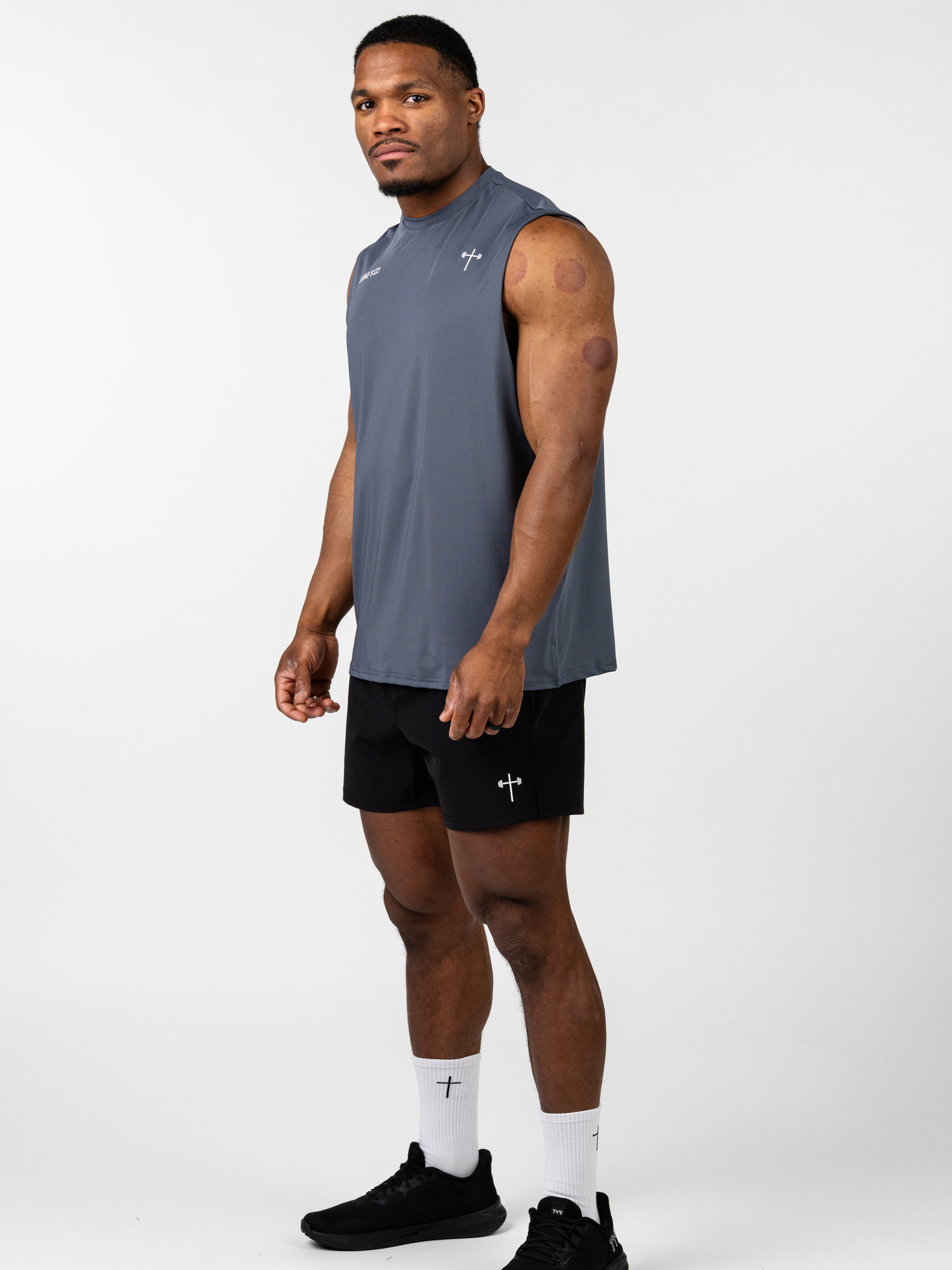 Athletic man wearing the Carry Your Cross Premium Oversized Tank in gray, paired with black shorts and white socks featuring a cross, showcasing Christian fitness apparel.