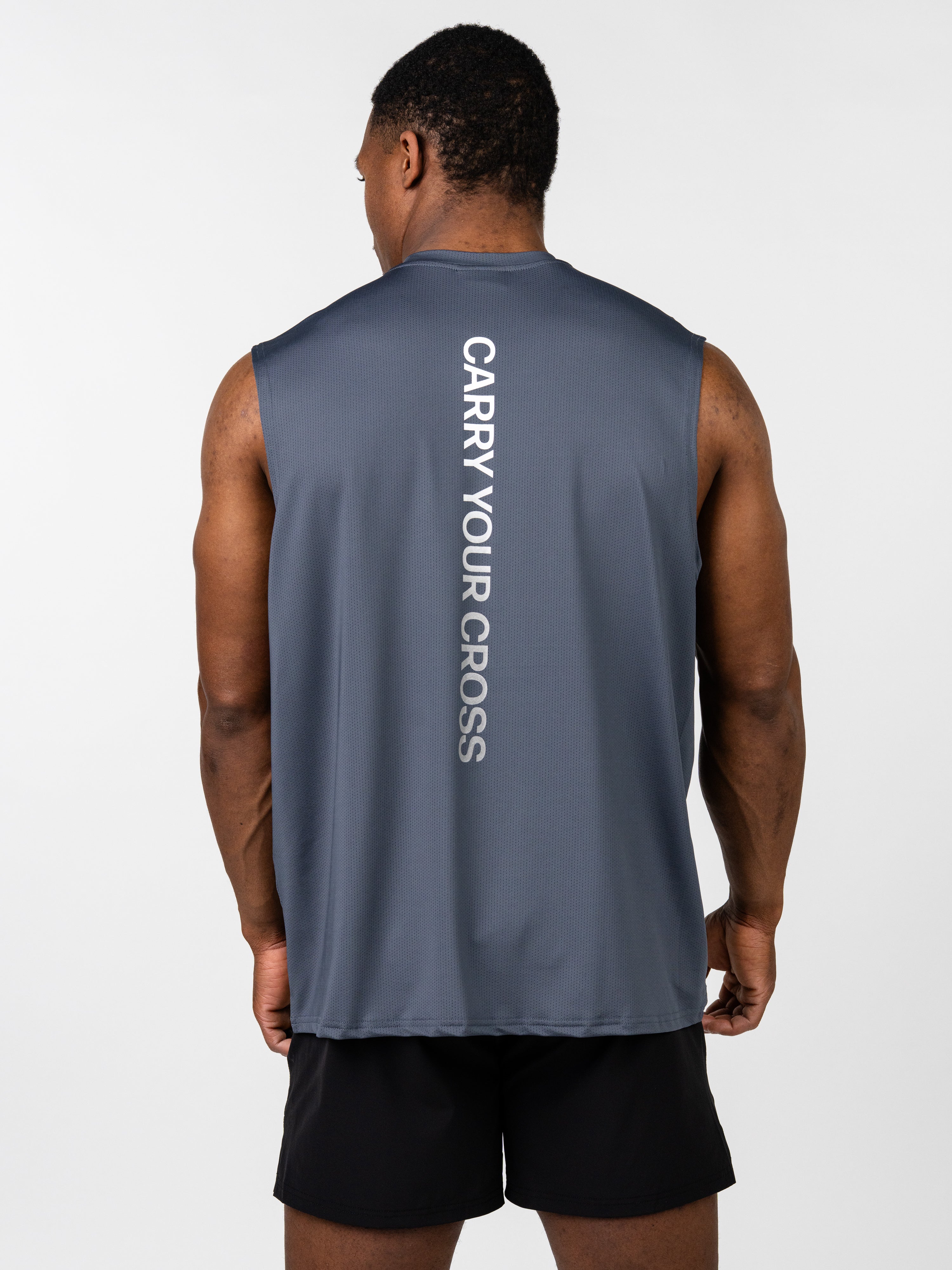 Male model wearing a dark blue Carry Your Cross Premium Oversized Tank with a vertical "CARRY YOUR CROSS" text on the back, paired with black athletic shorts.