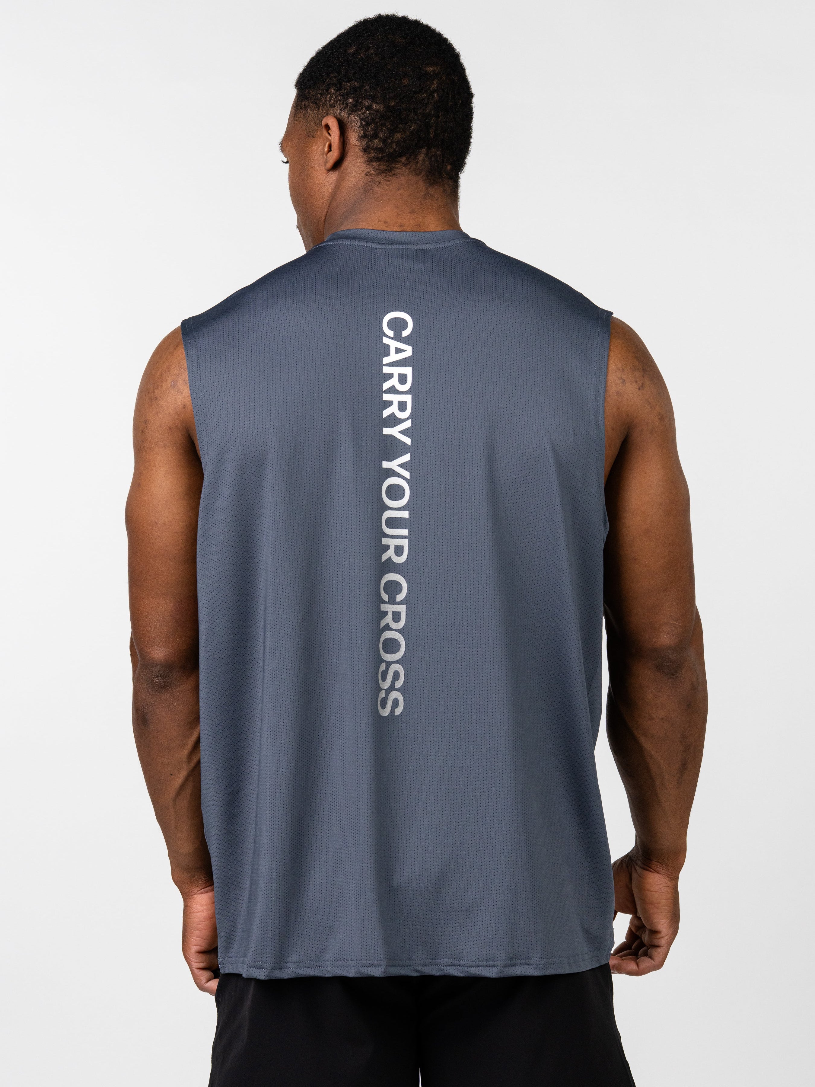 Male model wearing a dark blue Carry Your Cross Premium Oversized Tank with a vertical "CARRY YOUR CROSS" text on the back, paired with black athletic shorts.