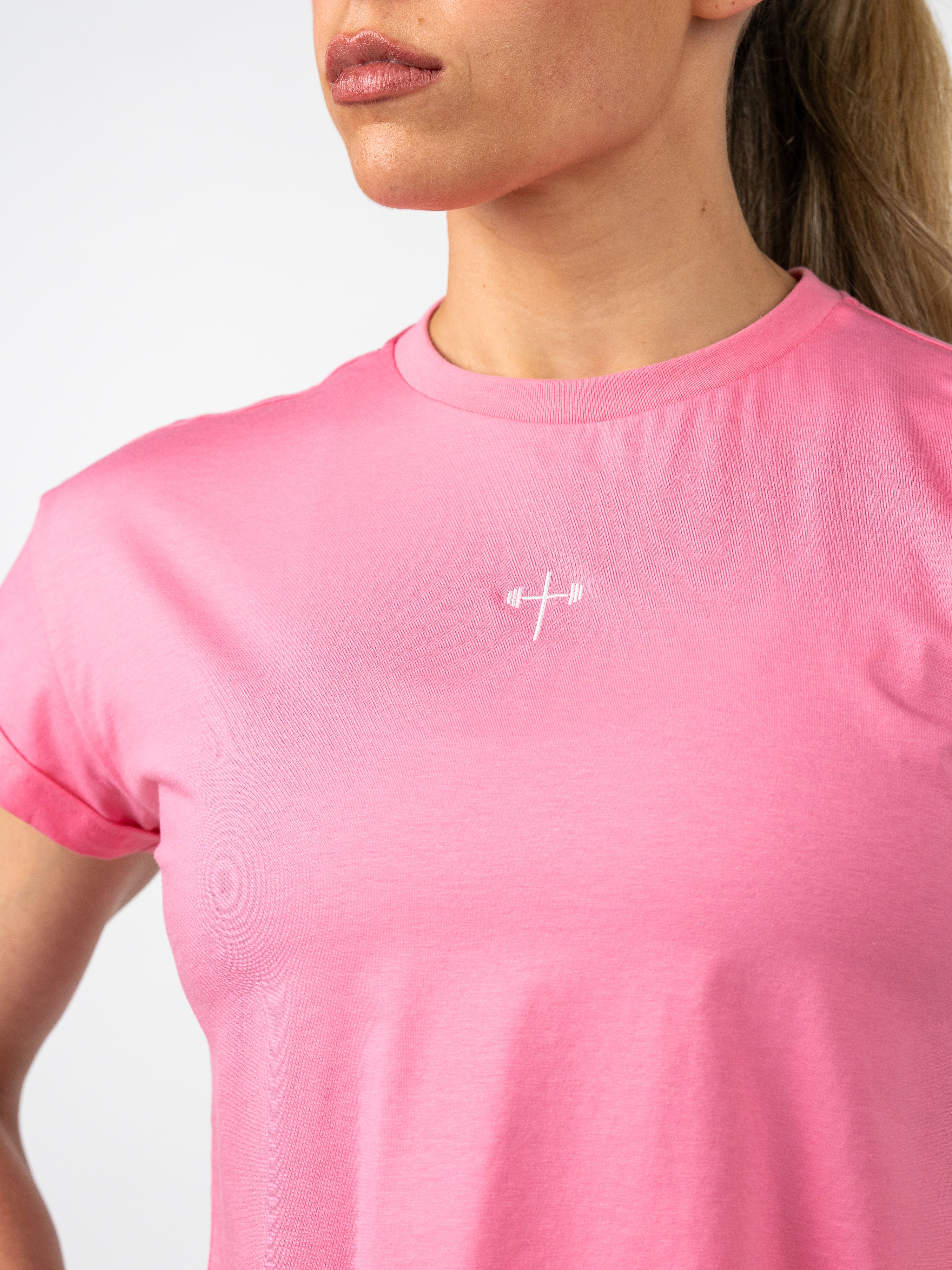 Close-up of a woman wearing a pink Cross Essential Crop Tee featuring a small white Christian cross with a barbell design on the chest, blending faith and fitness in activewear.