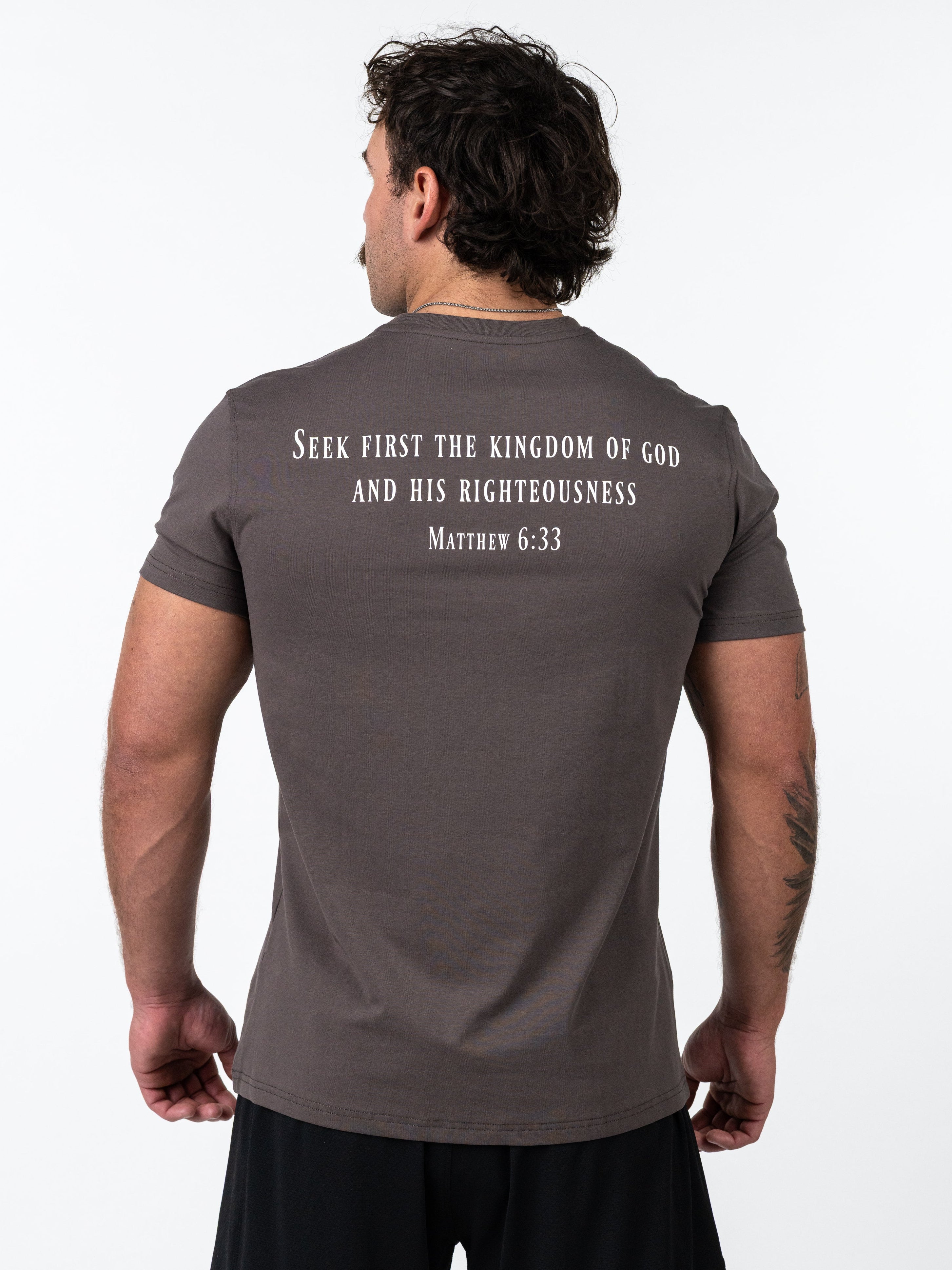 Man wearing an iron grey Sovereign Performance Tee with a printed Bible verse from Matthew 6:33 on the back, highlighting Christian gym clothing and faith-based fitness apparel.