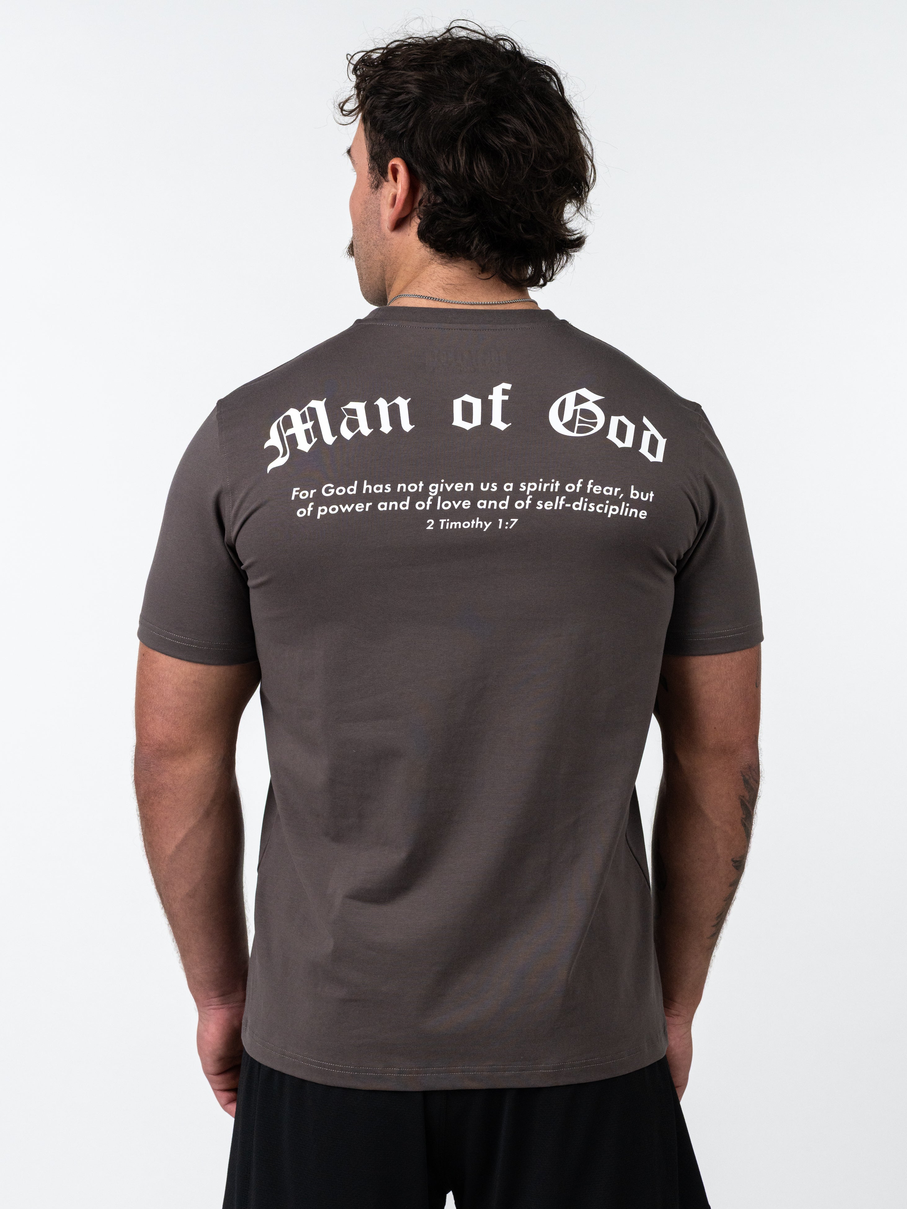 Man wearing a Kingdom Performance Tee in iron grey with white "Man of God" text and Bible verse on the back, standing facing away against a plain background.