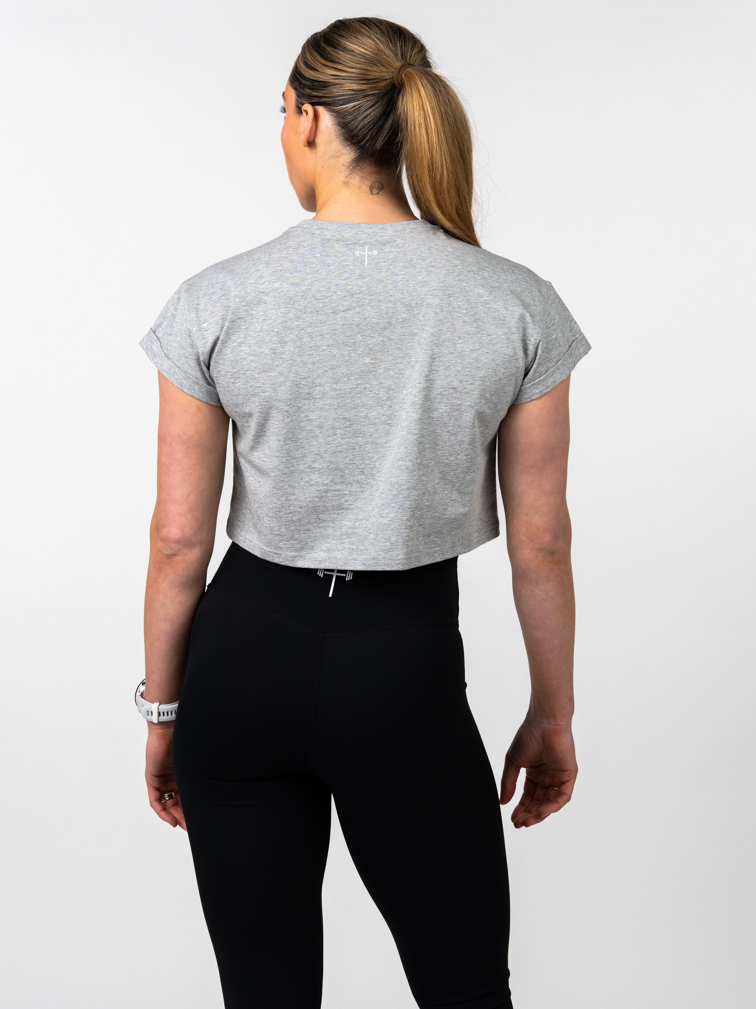 Person wearing a gray crop top and black leggings on a white background