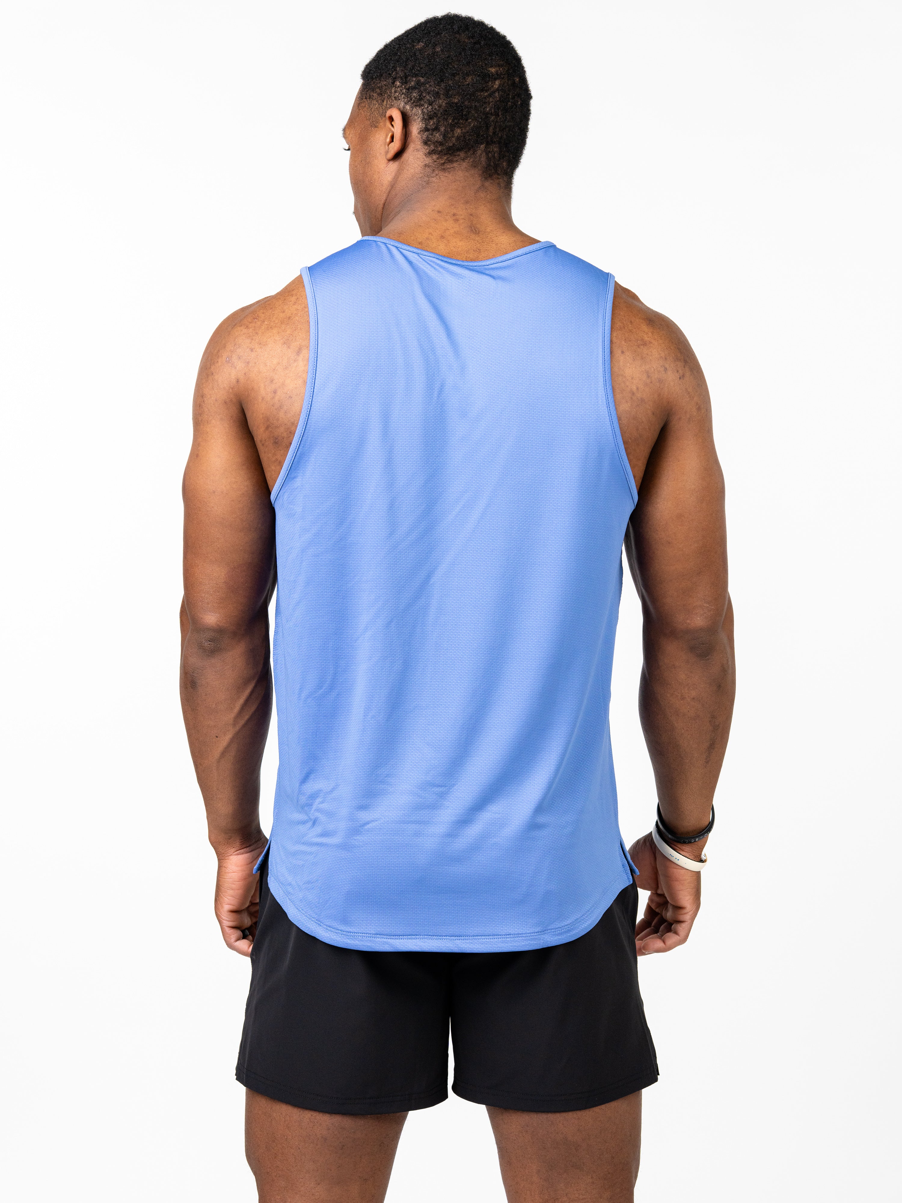 Man wearing a light blue Signature Tank sleeveless performance tee with 4-way stretch fabric, paired with black athletic shorts, shown from the back.