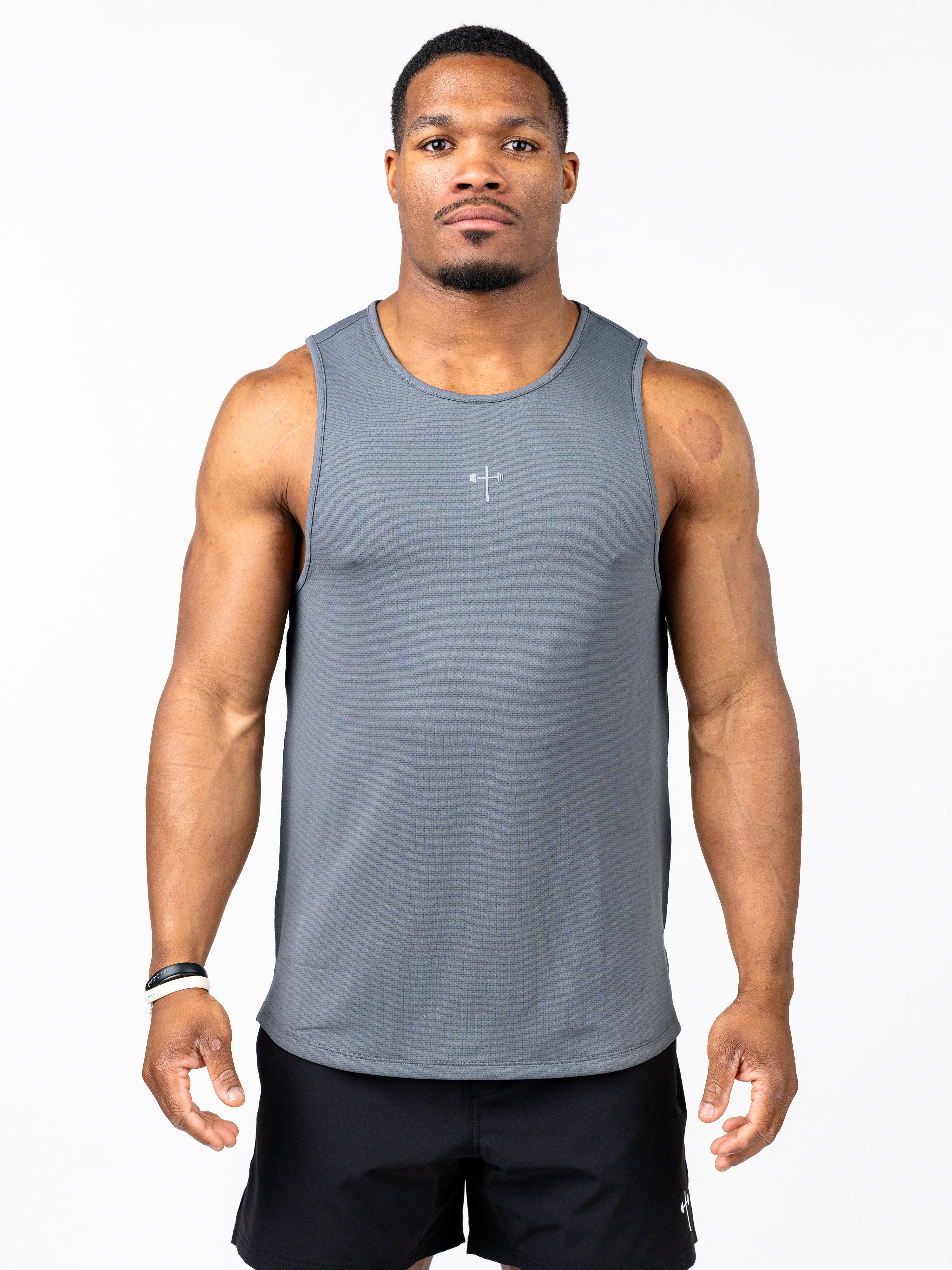 Male model wearing a gray Signature Tank with a subtle Christian cross and barbell design on the chest, styled for athletic performance and Christian fitness apparel.