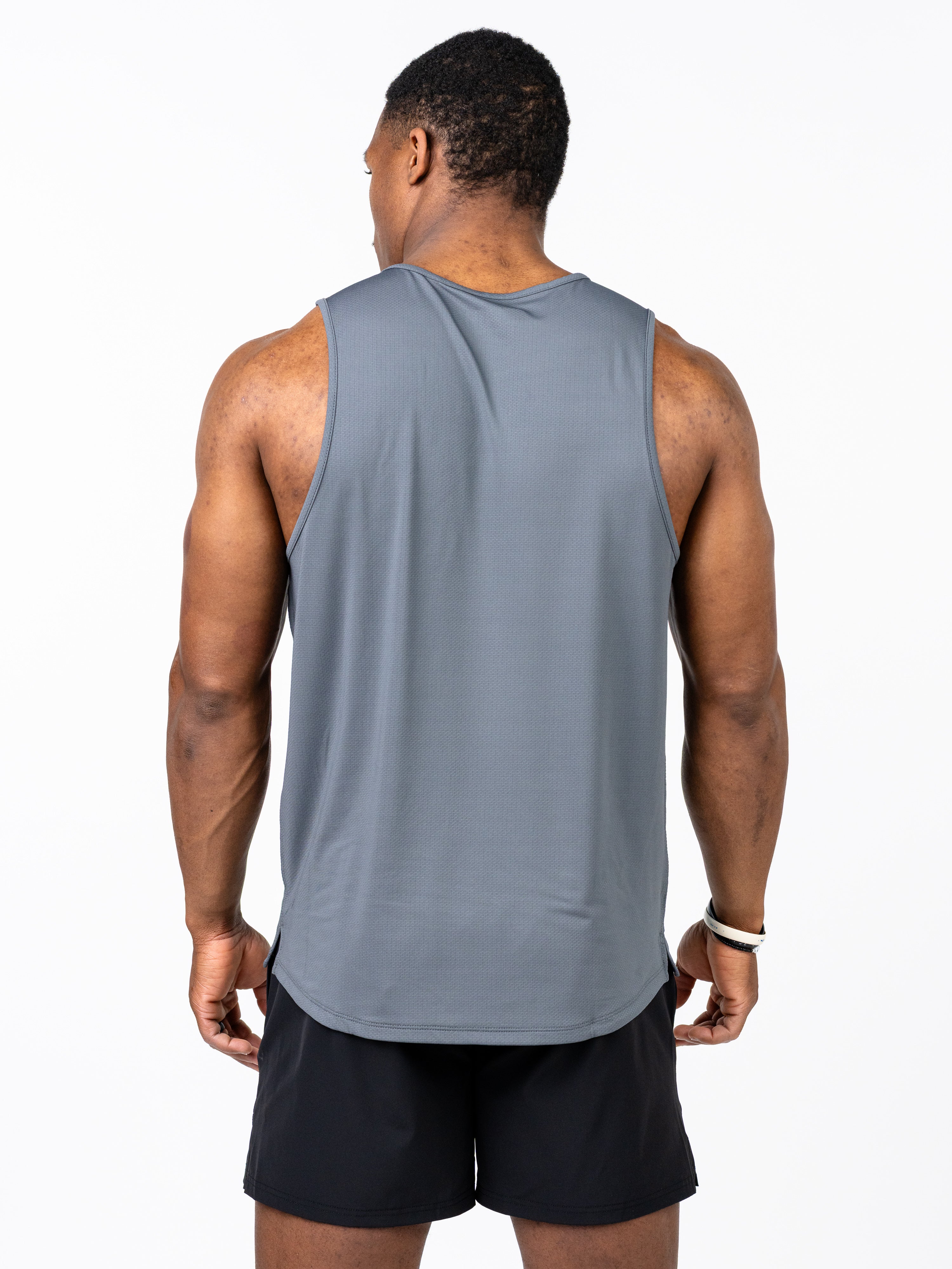 Man wearing a gray Signature Tank sleeveless performance top with breathable fabric, shown from the back, paired with black athletic shorts.
