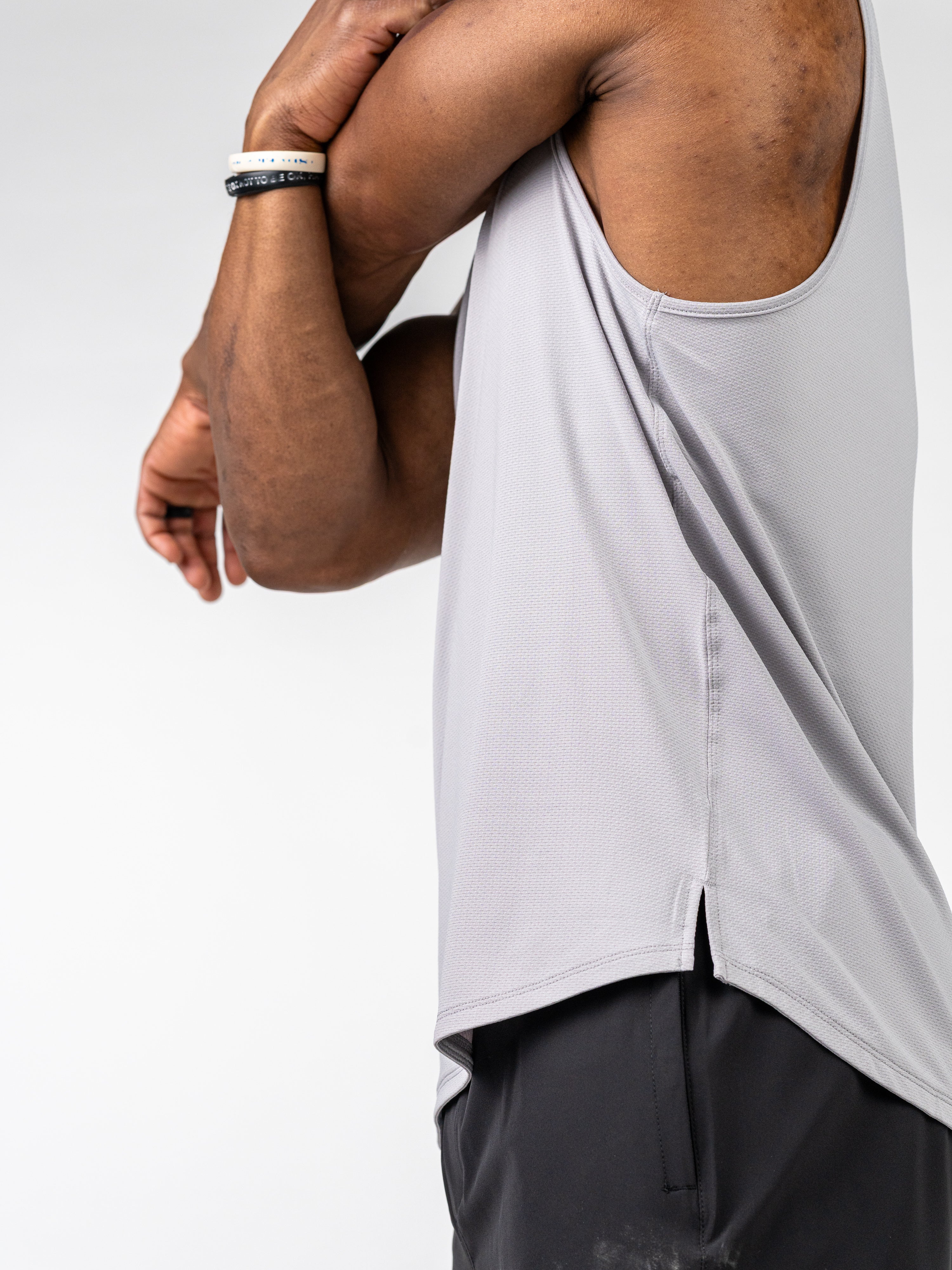 Man wearing a light grey Signature Tank stretching his arm, showcasing the breathable, sweat-wicking fabric designed for intense training and active movement.