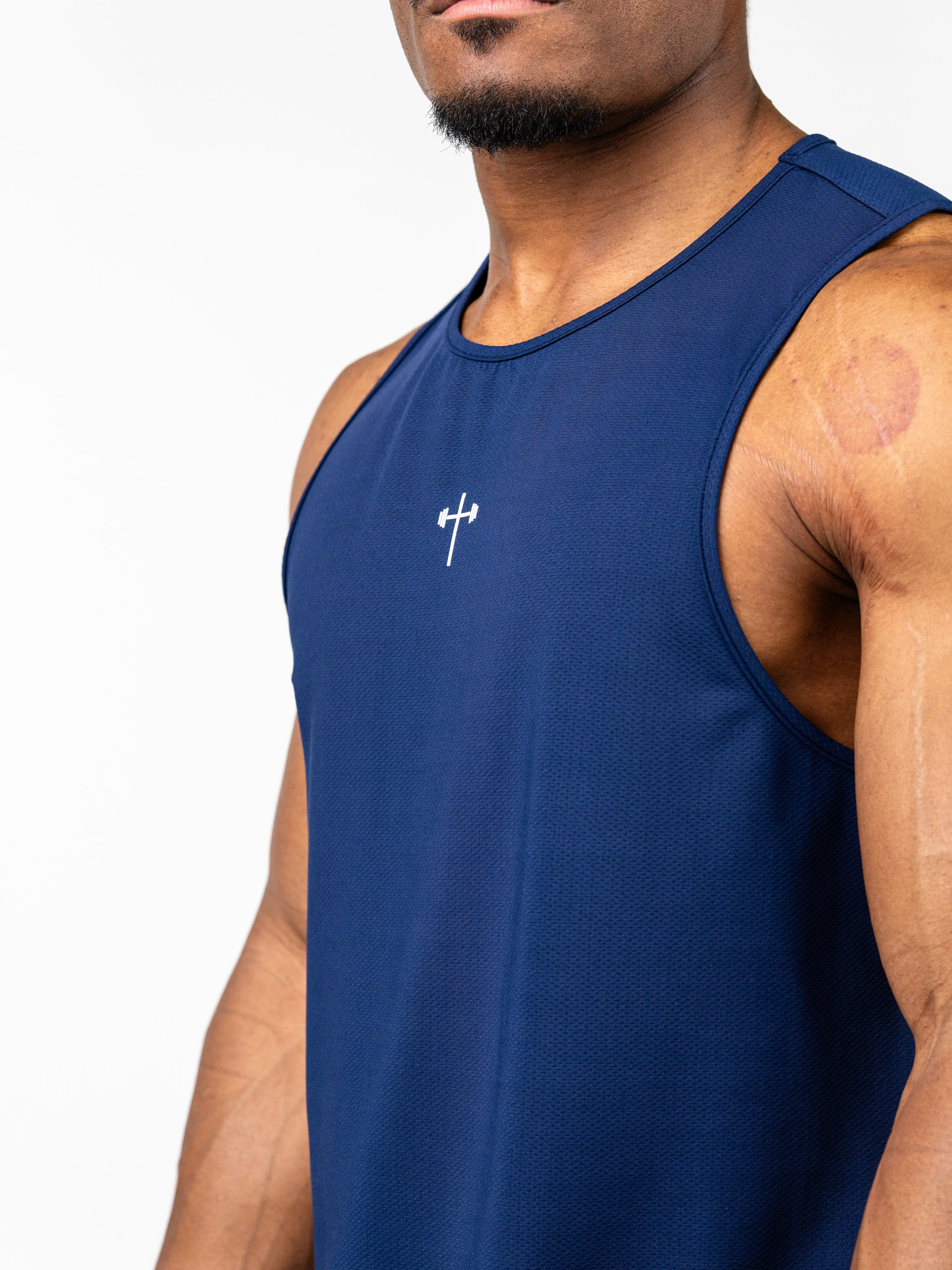 Close-up of a man wearing a navy blue Signature Tank with a small white Christian cross and barbell design on the chest, made from breathable, sweat-wicking fabric.
