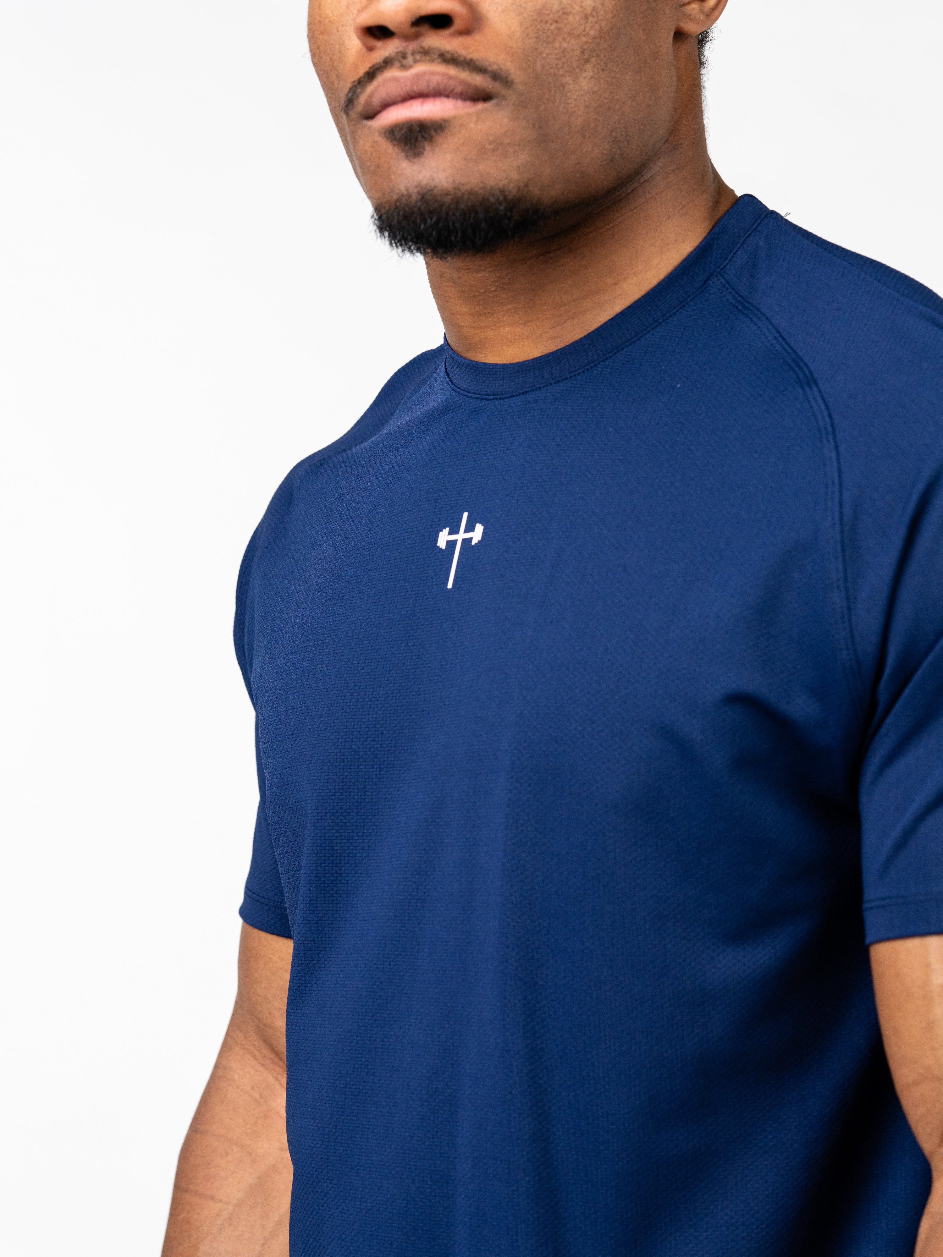 Man wearing a navy blue Signature Tee with a small white Christian cross and barbell design on the chest, made from breathable, sweat-wicking performance fabric.