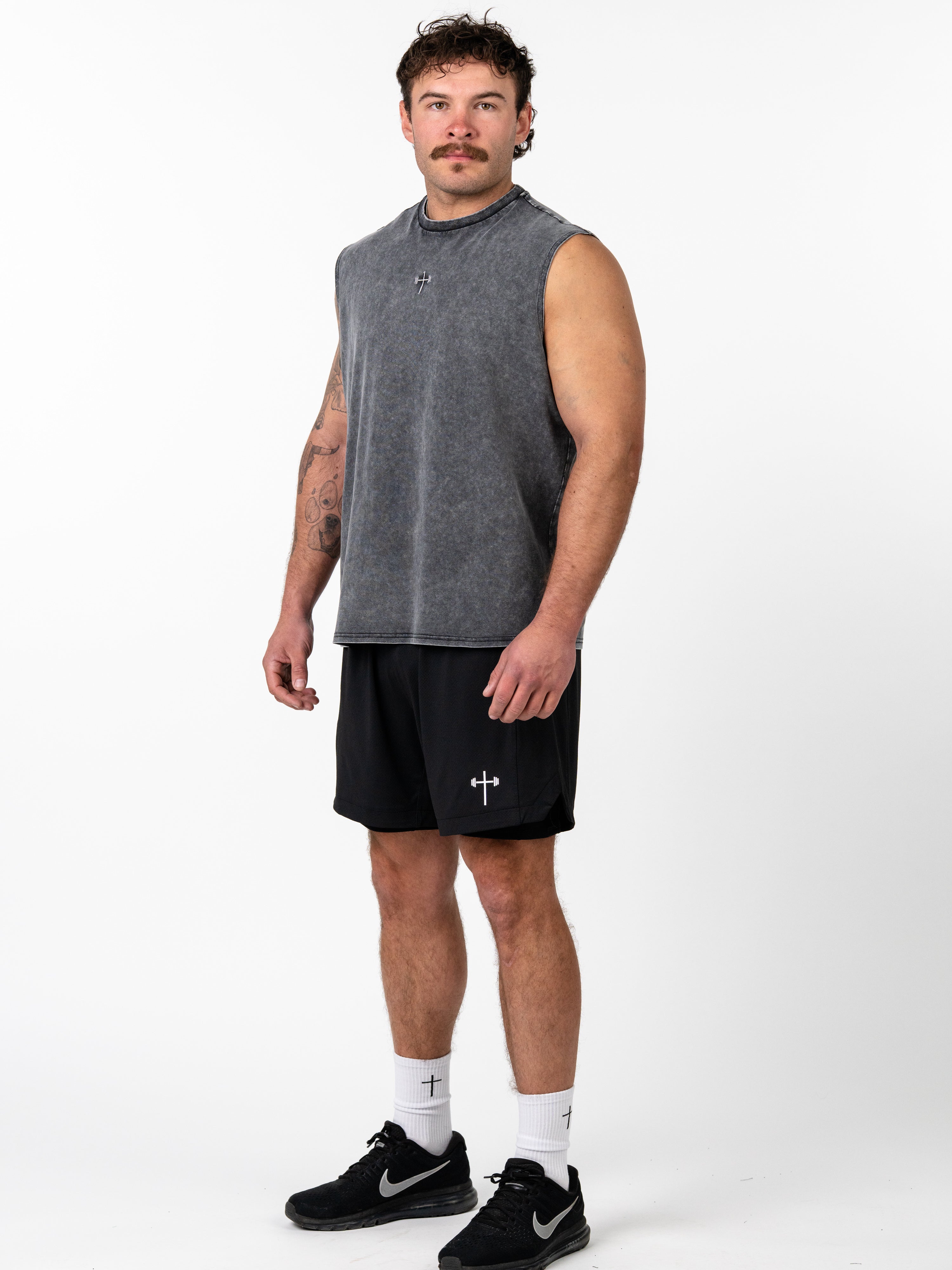 Man wearing God is Love Vintage Premium Tank in faded gray with black shorts and white socks, featuring Christian gym clothing with subtle cross and barbell design.