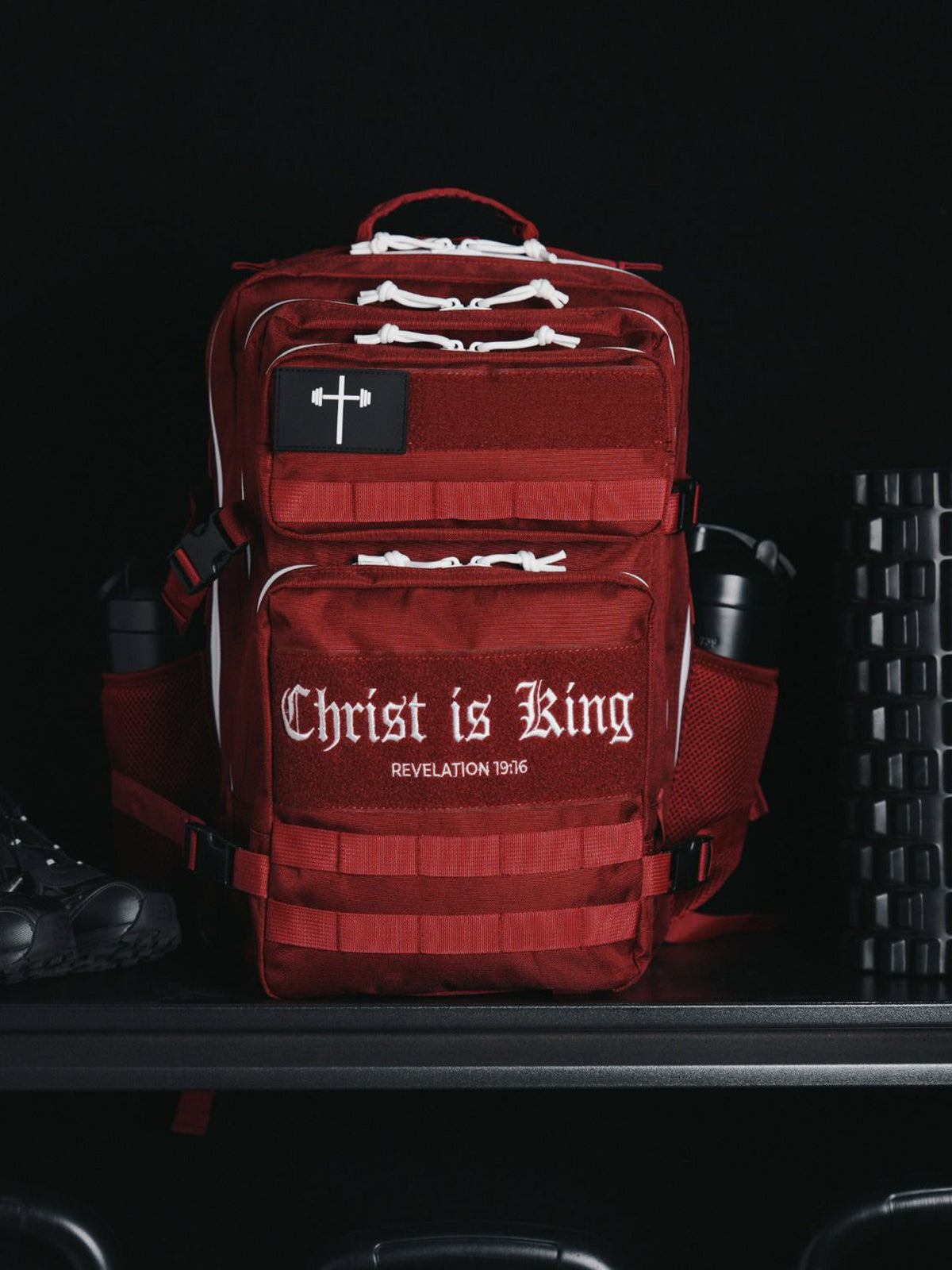 HolStrength 45L Tactical Backpack in red with multiple zippered compartments and a cross patch displayed beside gym equipment
