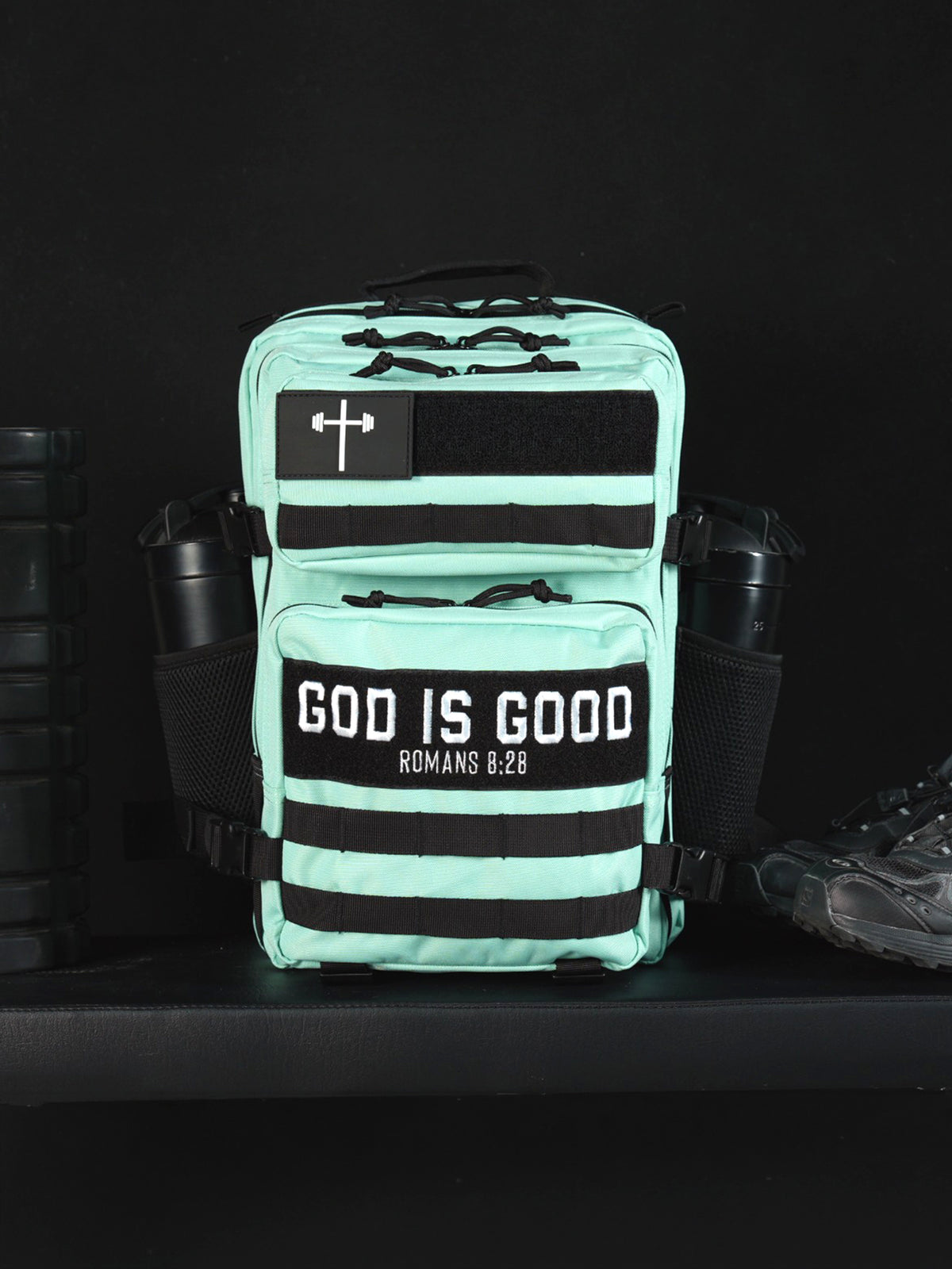 25L Tactical Backpack in mint green with multiple zippered compartments black straps cross patch and God Is Good panel displayed beside a water bottle