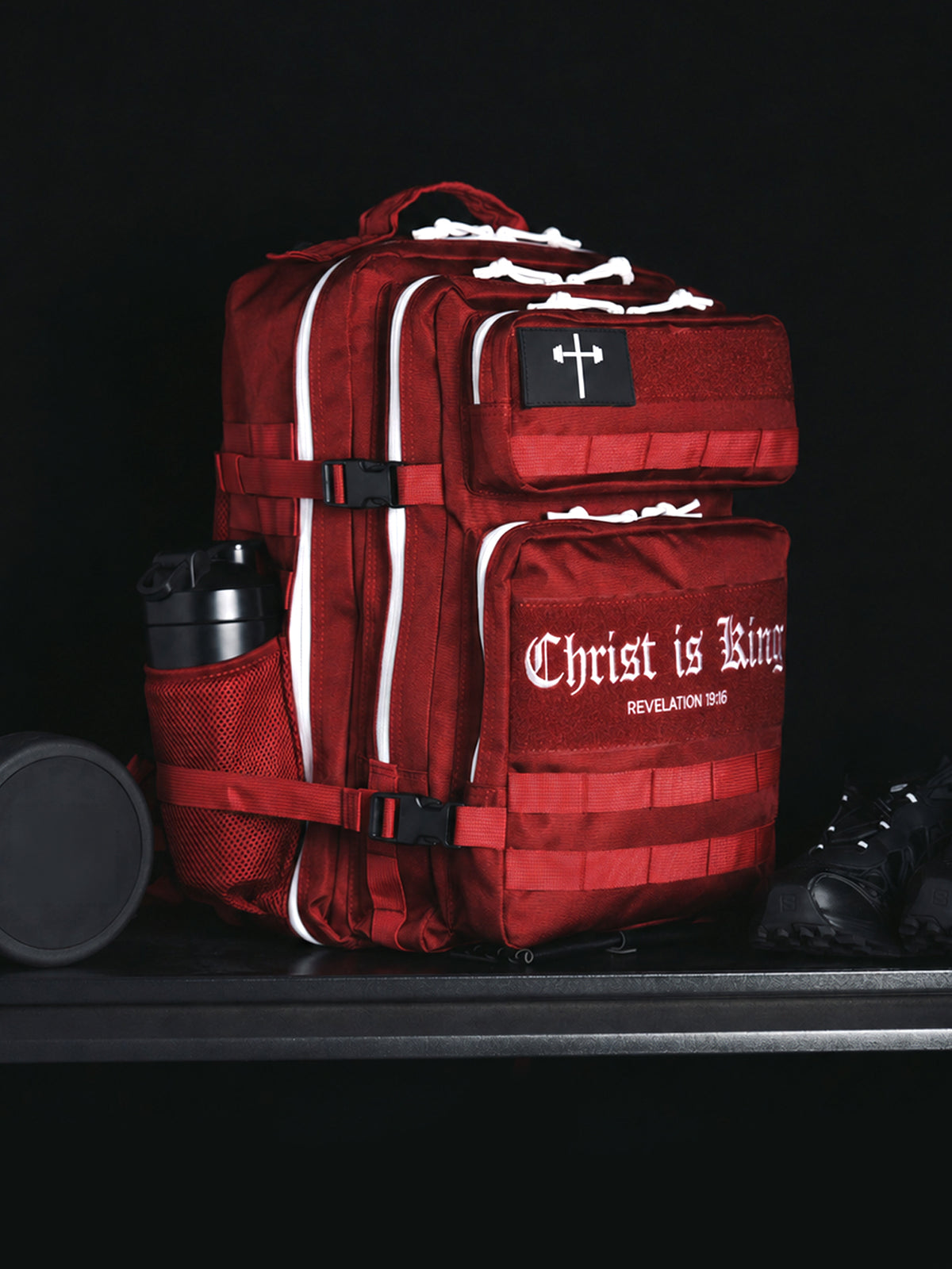 HolStrength 45L Tactical Backpack in red with multiple compartments, reflective accents, side bottle holder, and durable straps displayed with gym gear