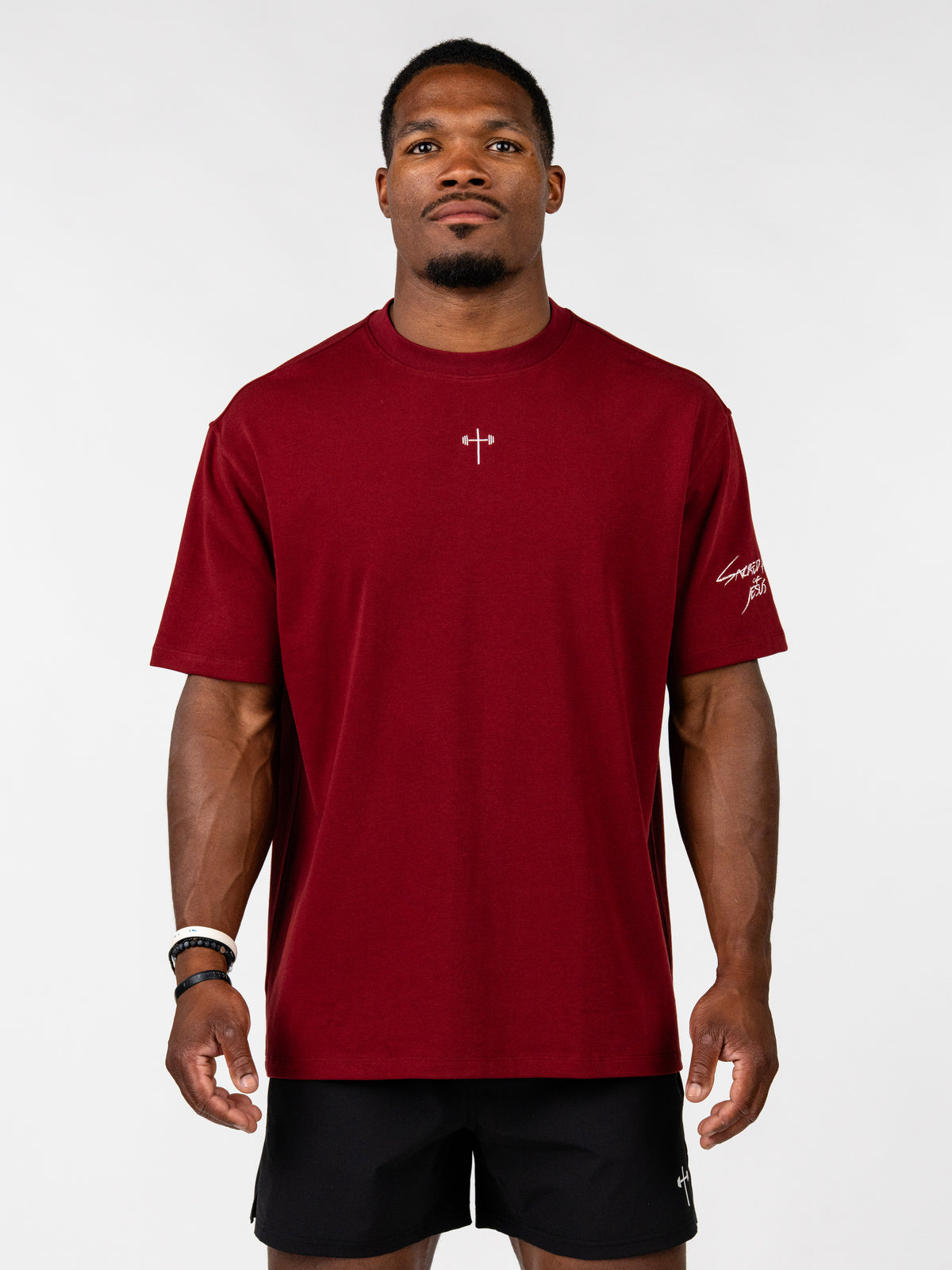 Sacred Heart Premium Oversized Tee in deep red with a subtle cross emblem and sleeve detail modeled as Christian fitness apparel for a bold faith based look