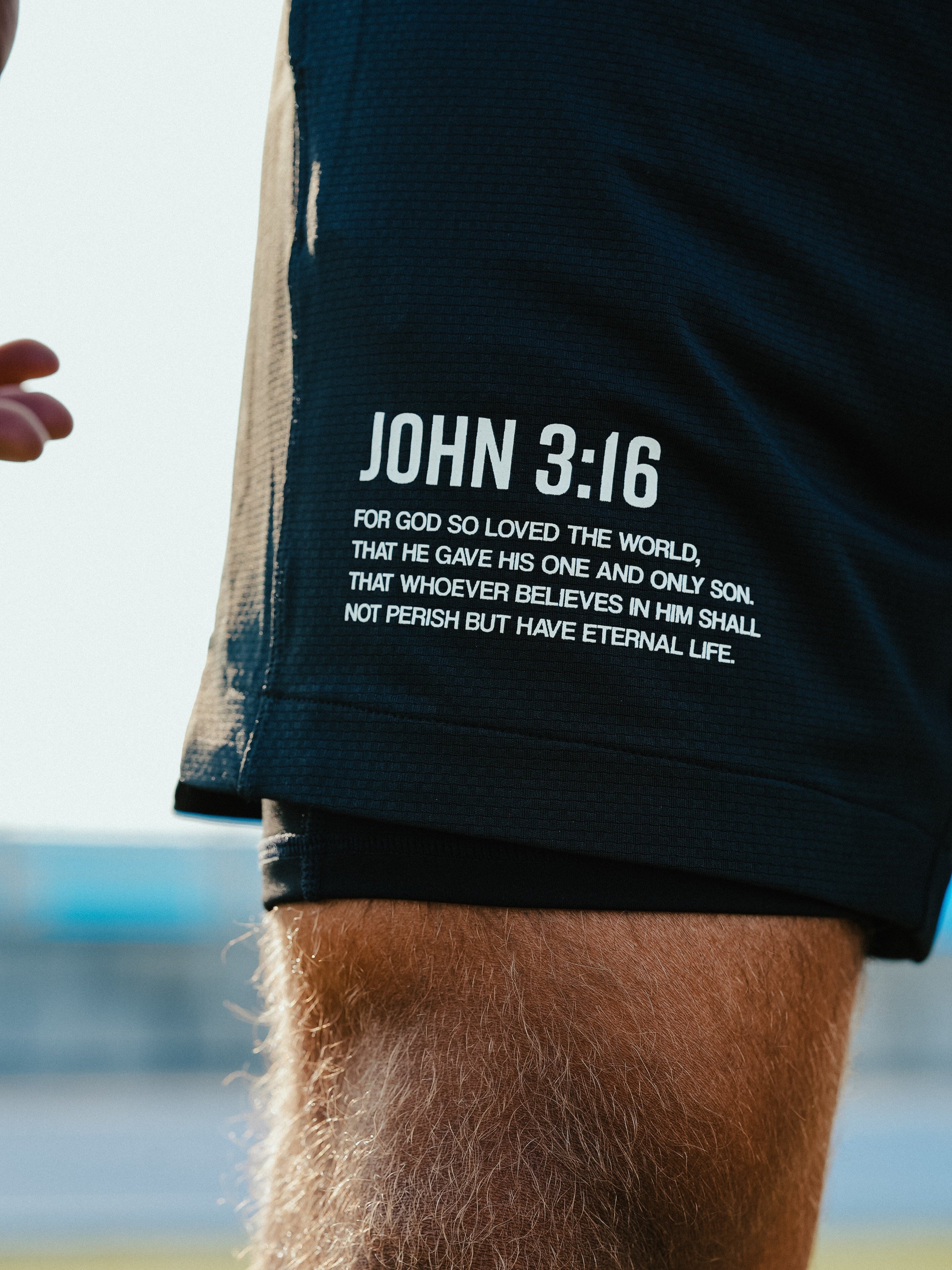 Person wearing black shorts with 'John 3:16' text, standing outdoors.