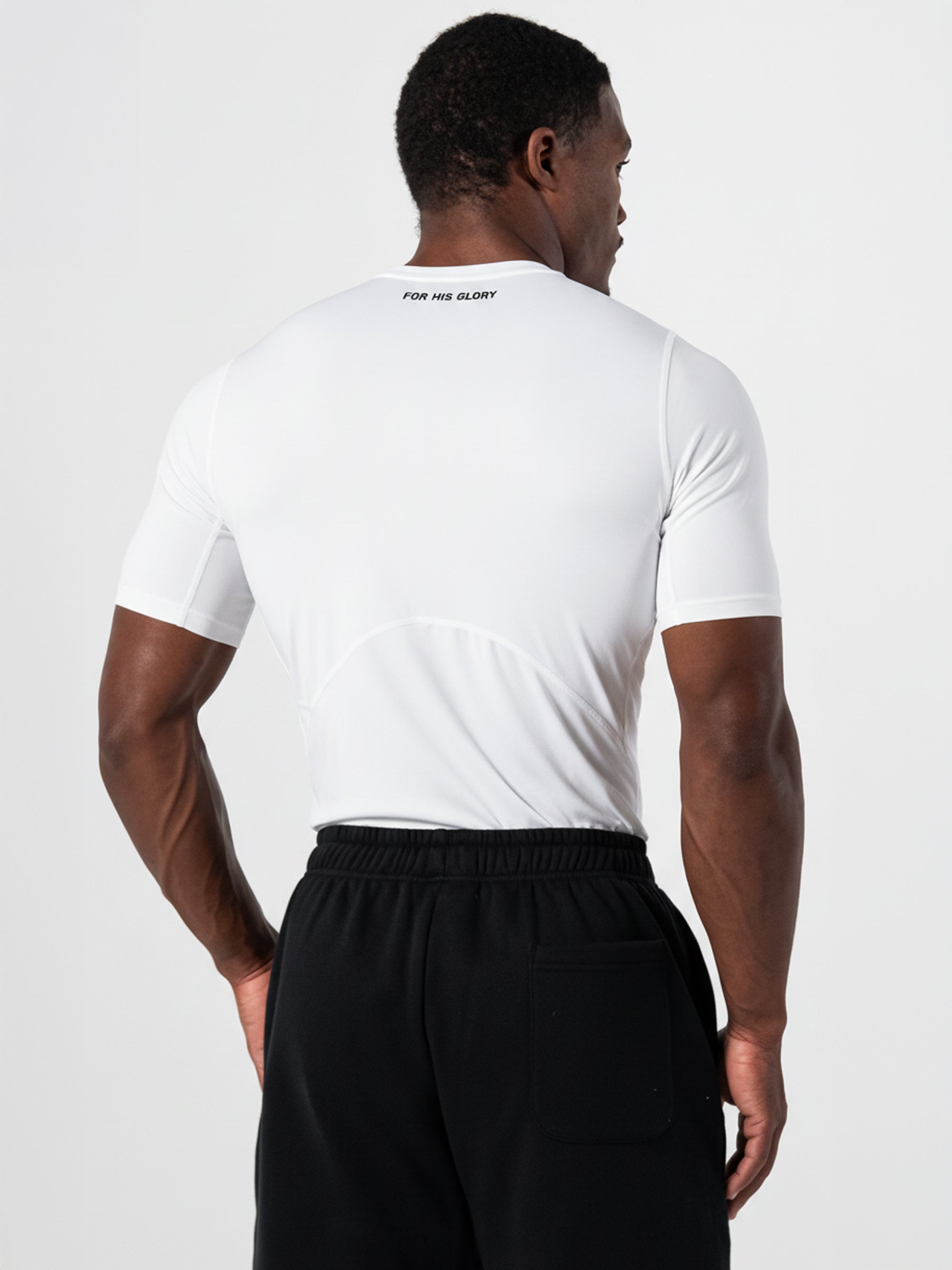 Athletic man wearing a white Core Base Layer Tee with a lightweight compression fit, shown from the back, paired with black athletic pants.