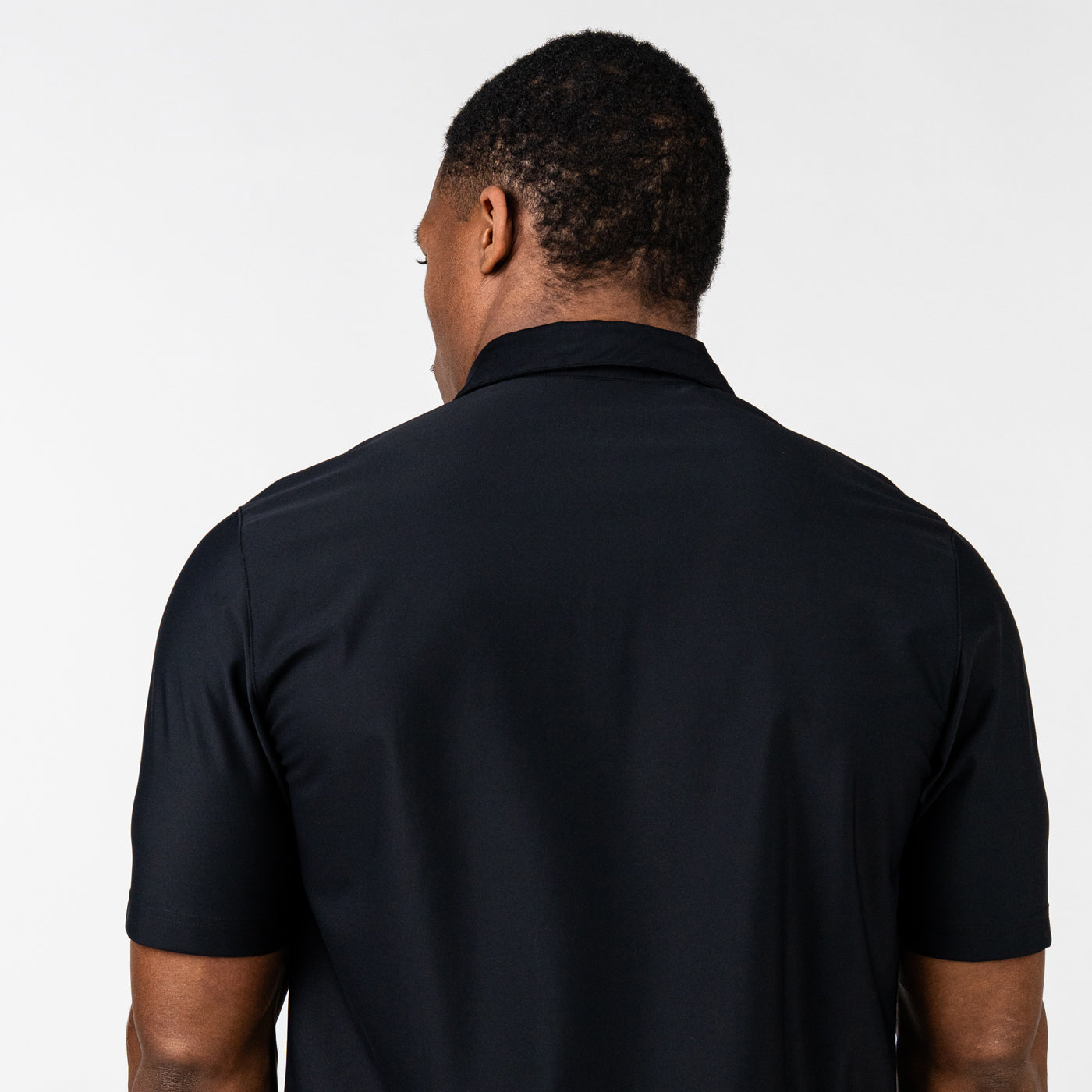Back view of a man wearing a plain black short-sleeve polo shirt against a white background.