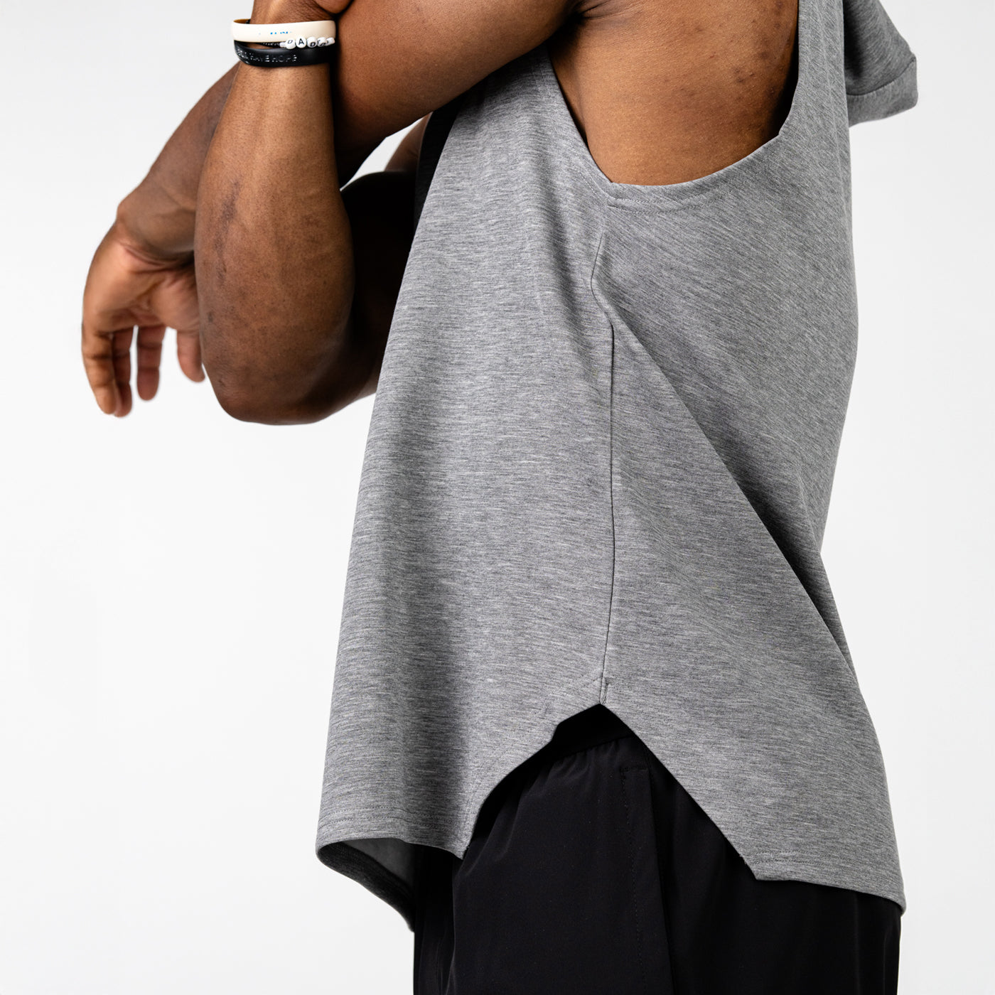 Close-up of a person wearing a sleeveless gray workout top and black athletic shorts, with their arm bent crossing their chest against a white background.