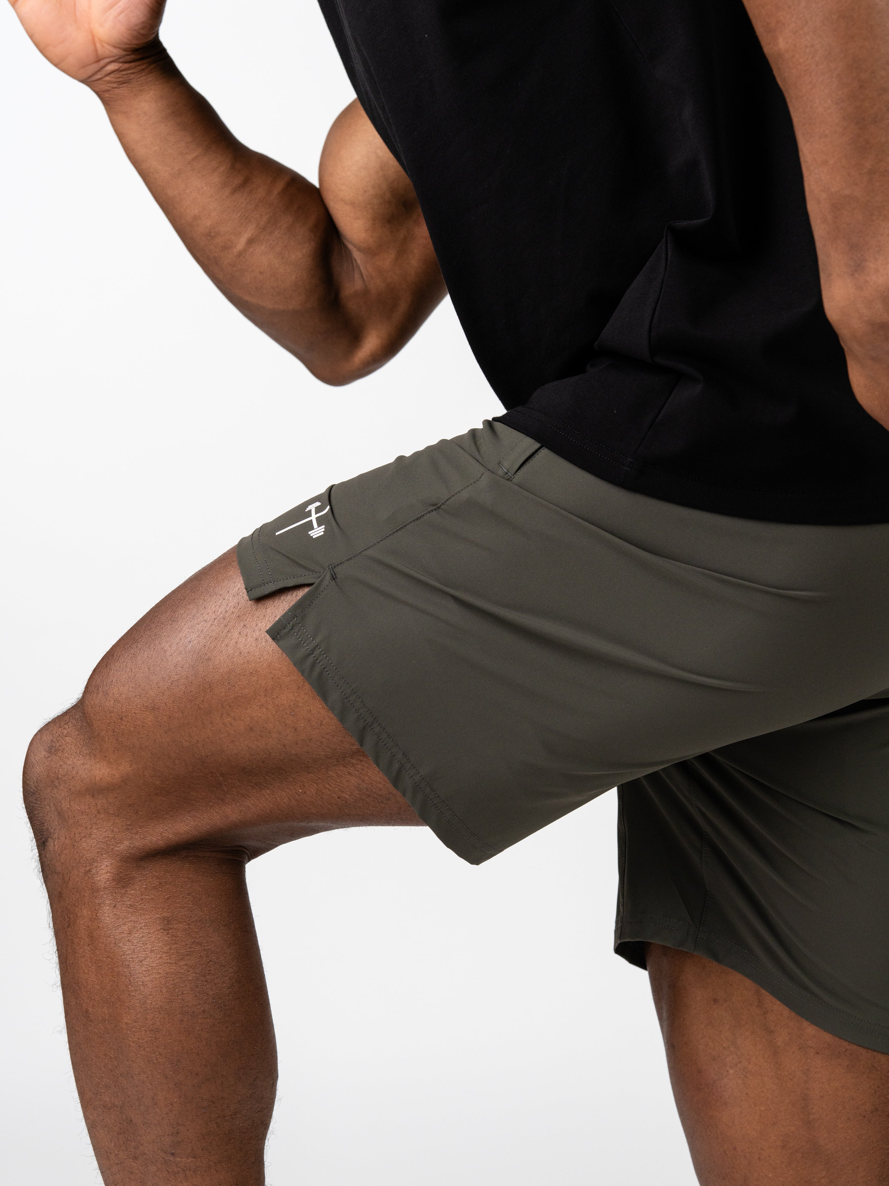 Close-up of a person wearing olive green Essential Training Shorts designed for movement and performance, paired with a black top showcasing a Christian-inspired logo on the shorts.