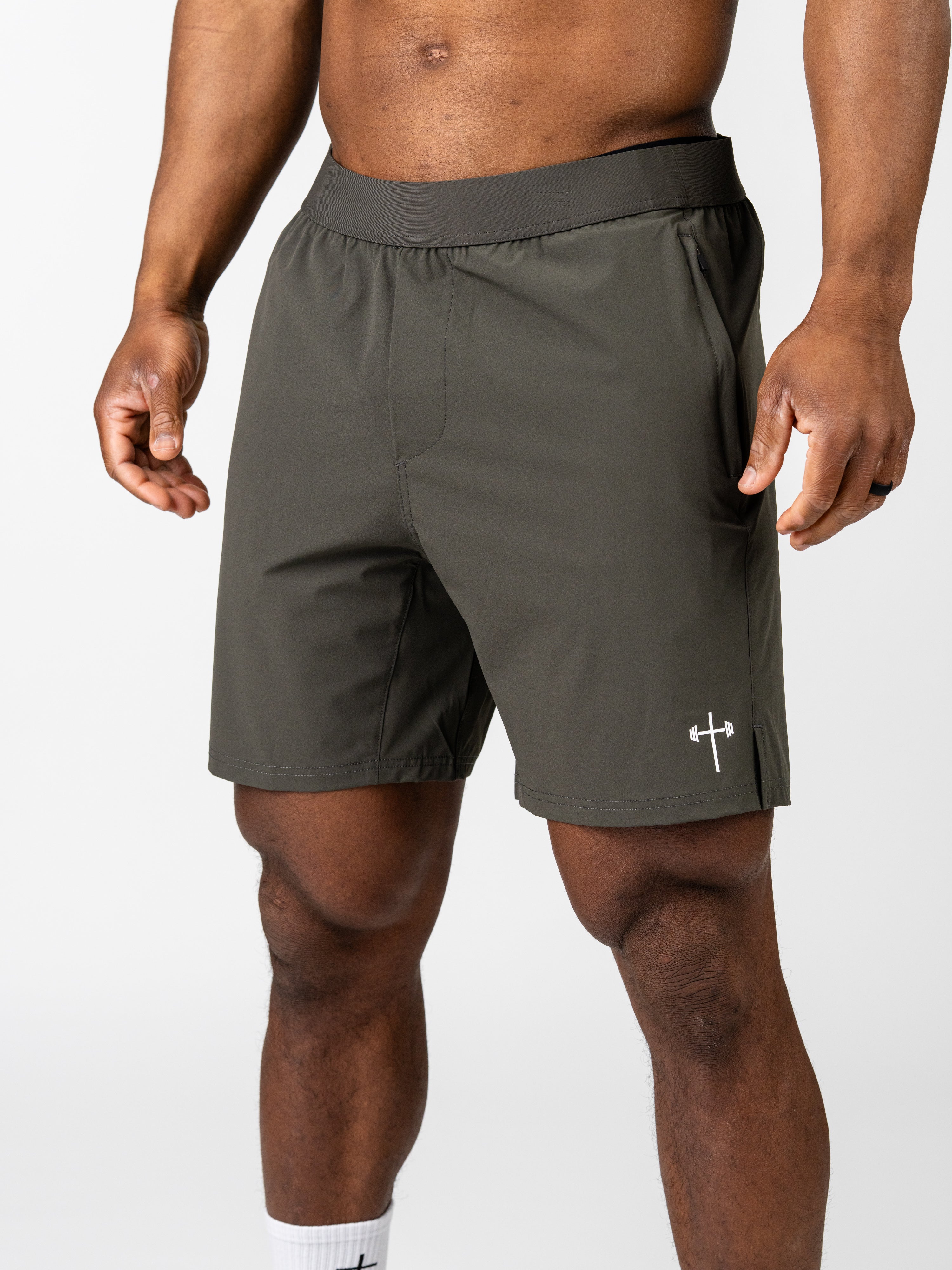 Athletic man wearing olive green Essential Training Shorts featuring a small white cross and barbell logo, designed for faith based fitness and Christian gym clothing.