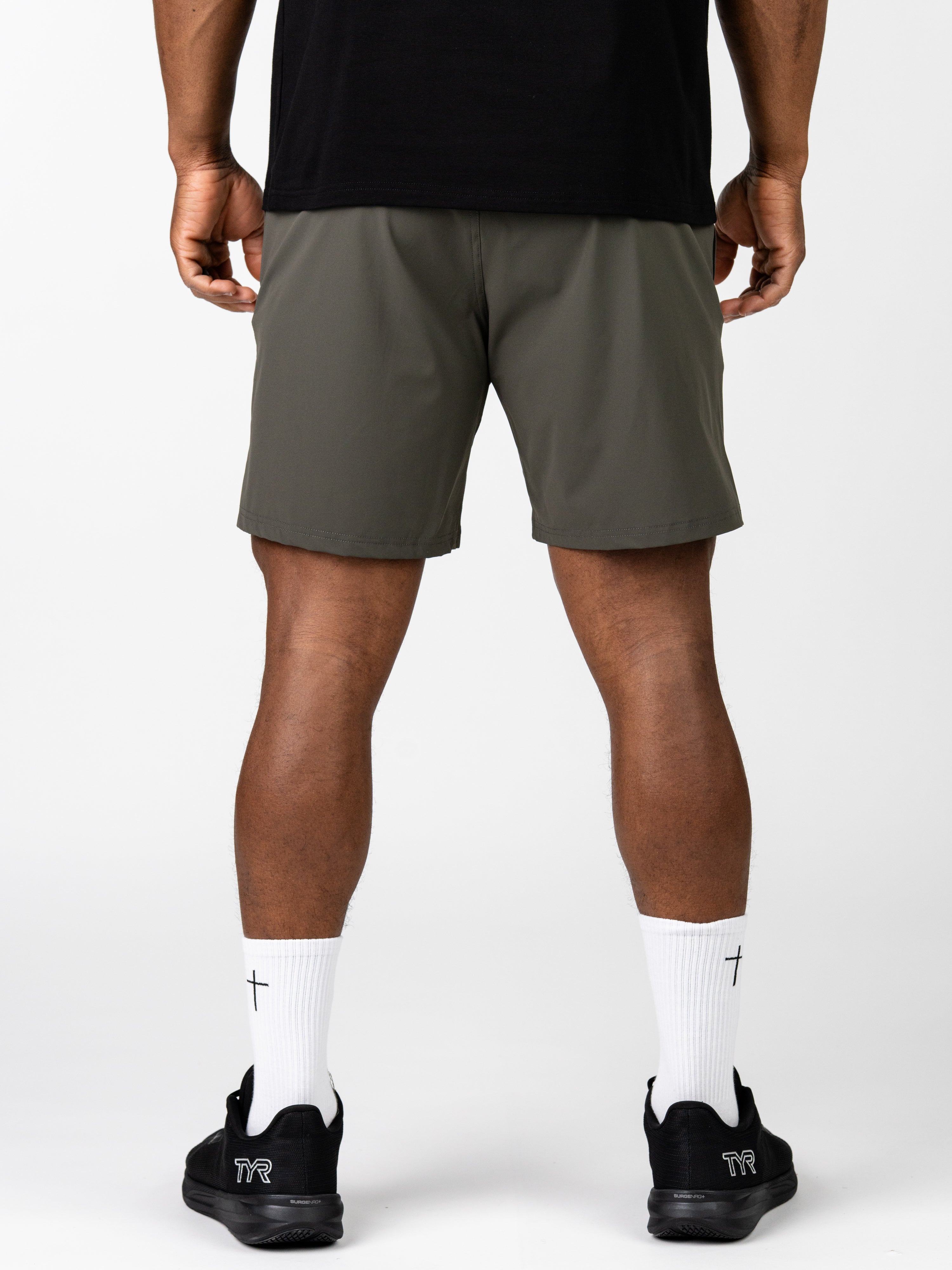 Rear view of a person wearing olive green Essential Training Shorts paired with white crew socks featuring a small black cross and black athletic shoes, showcasing comfortable Christian fitness apparel.