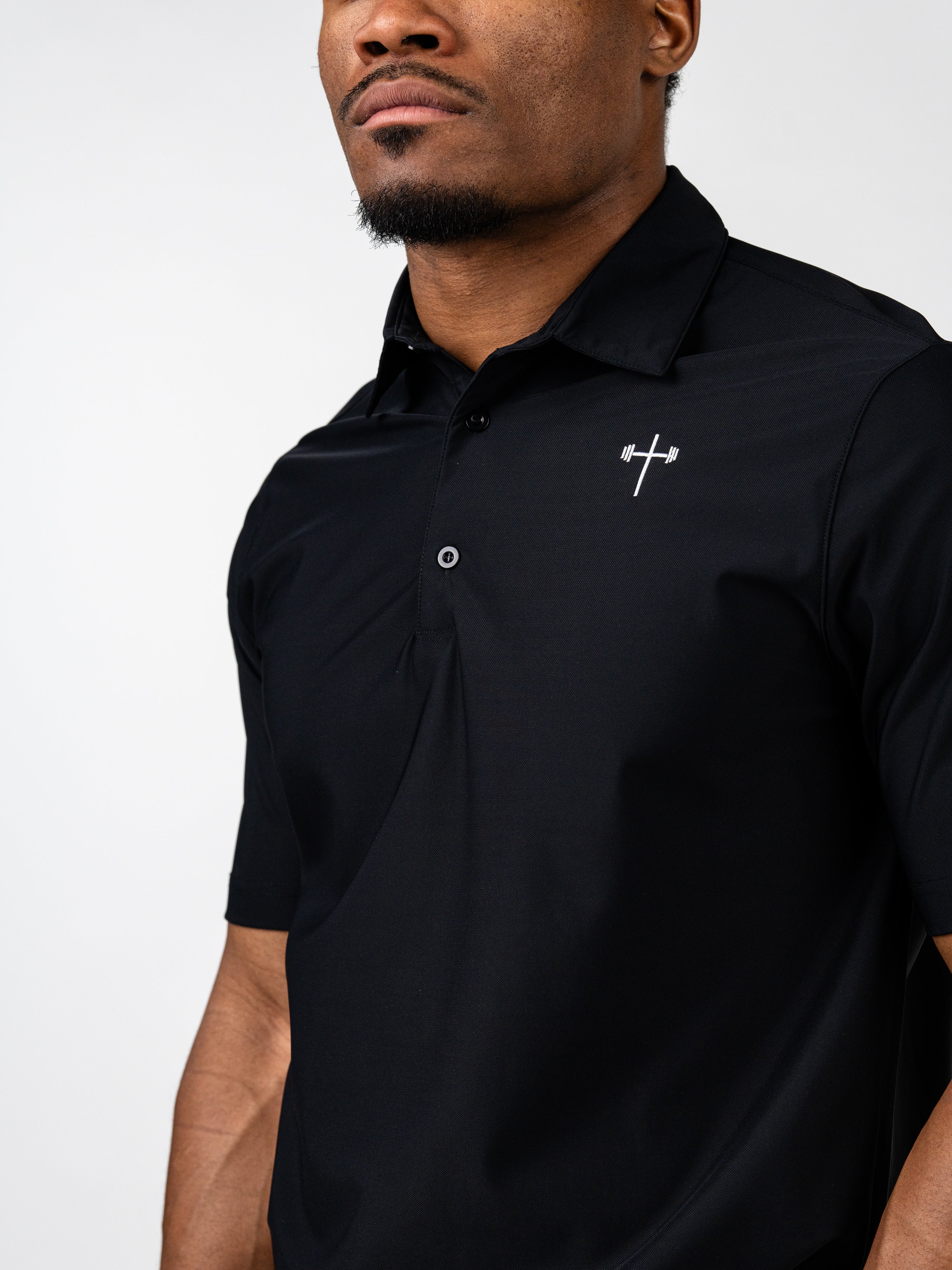 Man wearing a black Core Athletic Polo featuring a small white cross and barbell logo on the chest, combining Christian fitness apparel with performance and style.