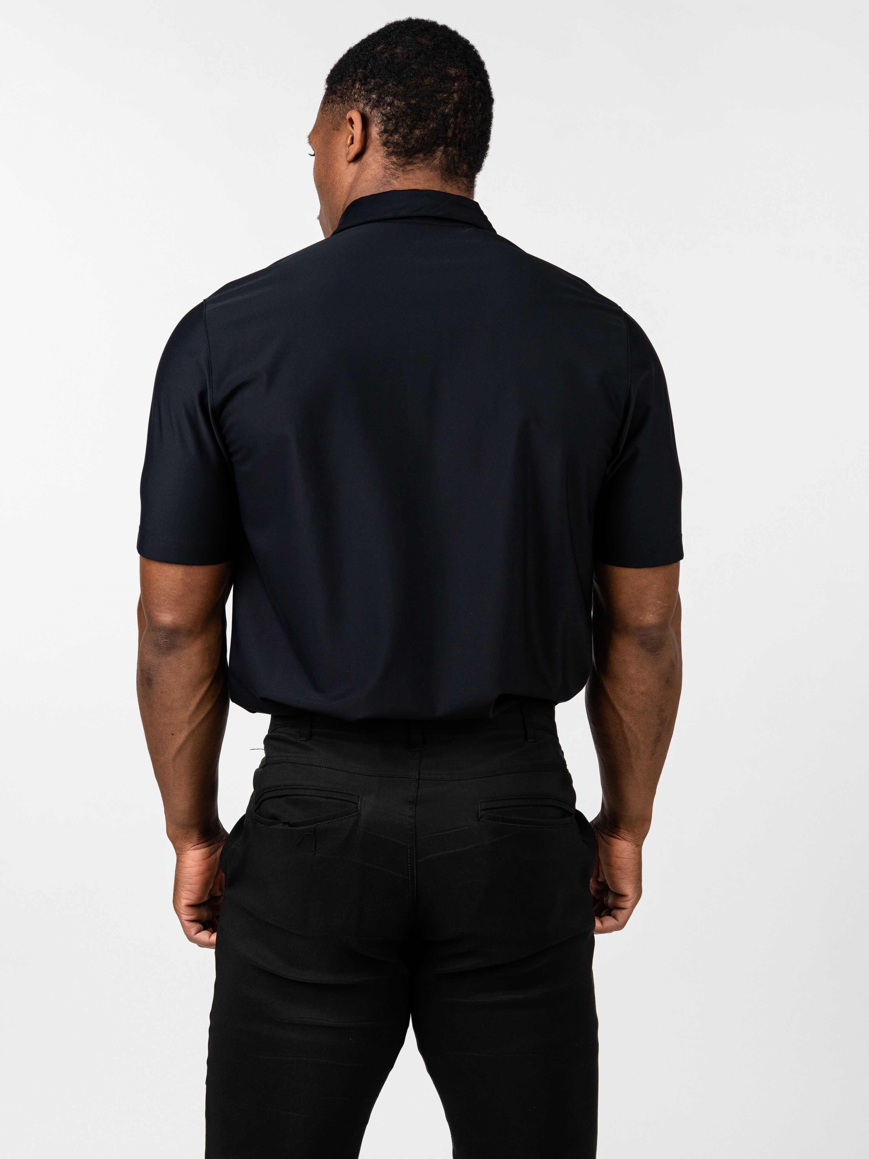 Man wearing black Core Athletic Polo standing with his back to the camera, showcasing the smooth, fitted fabric designed for comfort and athletic movement.