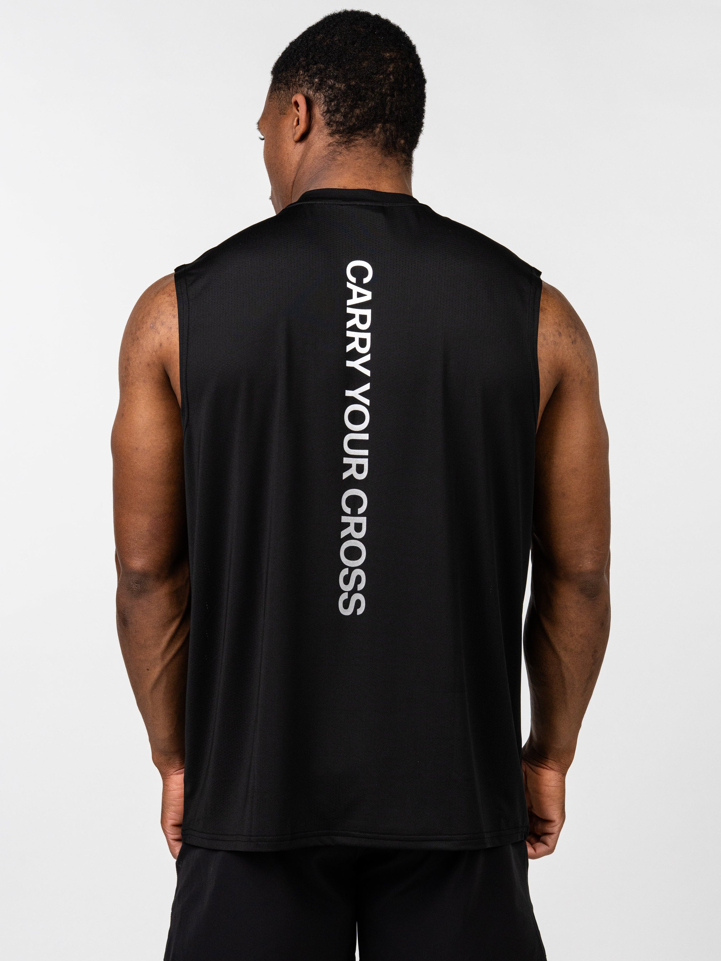 Man wearing the Carry Your Cross Premium Oversized Tank in black, shown from the back, featuring vertical white text "CARRY YOUR CROSS" on a sleeveless athletic shirt.