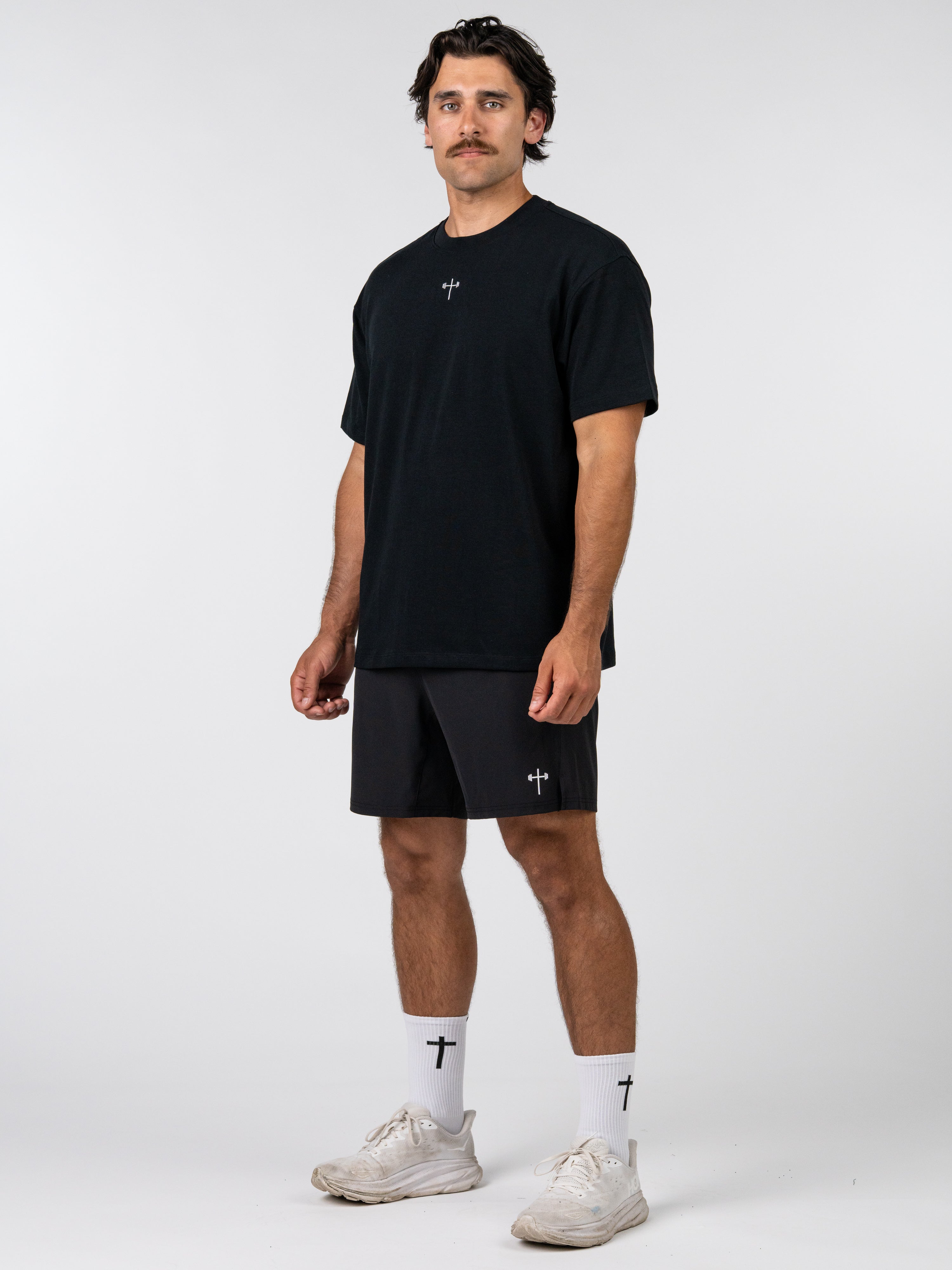 Man wearing a black t-shirt and shorts with a white background