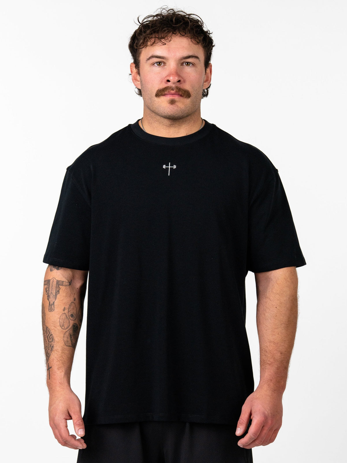 Man wearing a black Classic Oversized Tee featuring a small silver Christian cross with barbell design on the chest, styled for a relaxed, comfortable fit.
