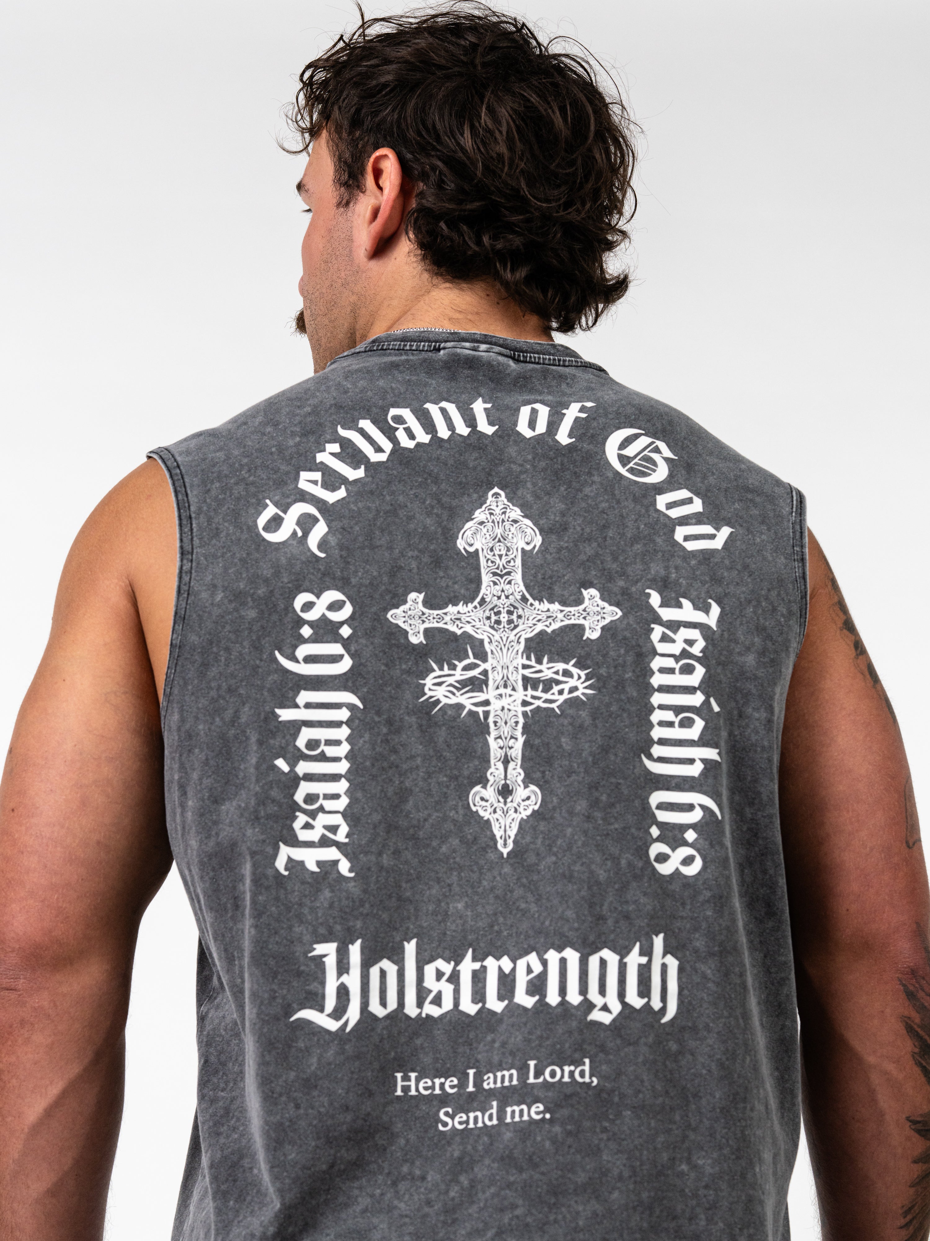 Man wearing a black washed sleeveless shirt with white text "Servant of God," "Isaiah 6:8," and "Holstrength" surrounding an ornate cross with a crown of thorns, featuring the phrase "Here I am Lord, Send me" on the back of the Servant of God Vintage Premium Tank.