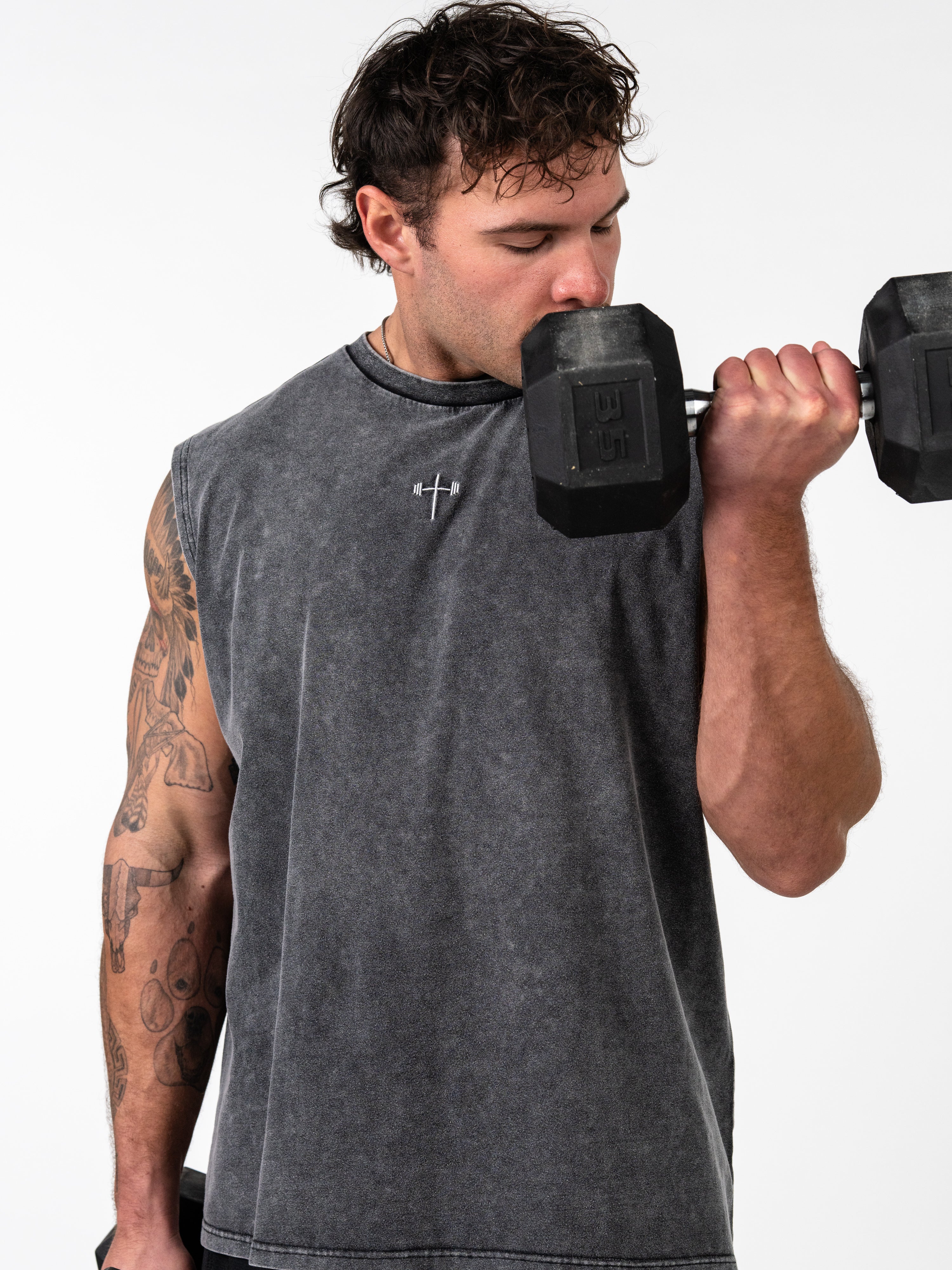 Man lifting a dumbbell wearing a faded black God is Love Vintage Premium Tank with a small embroidered cross and barbell design on the chest, showcasing Christian fitness apparel.