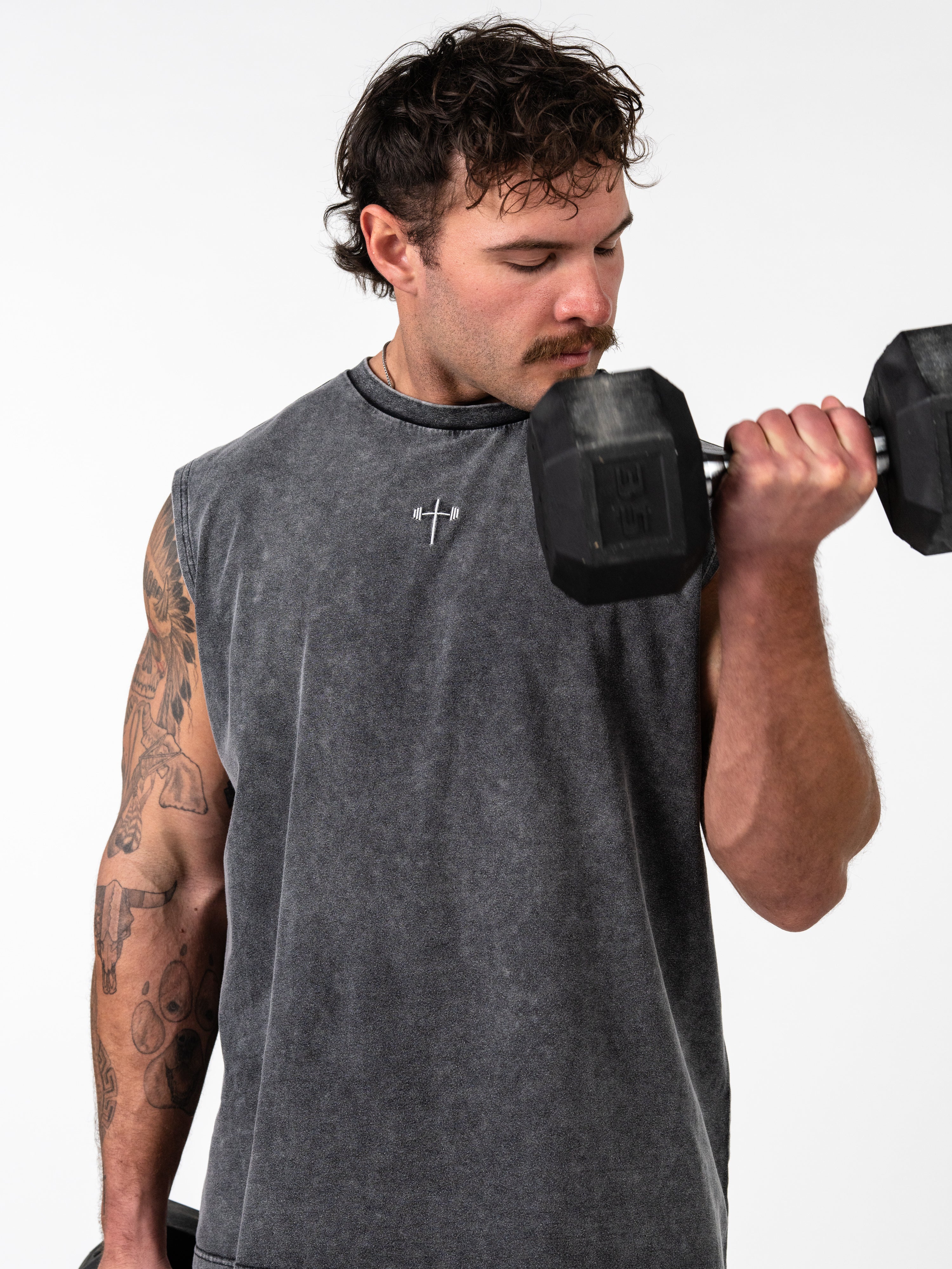 Man lifting a dumbbell wearing a gray Servant of God Vintage Premium Tank with a small cross and barbell design, representing Christian fitness apparel and faith-based workout clothes.